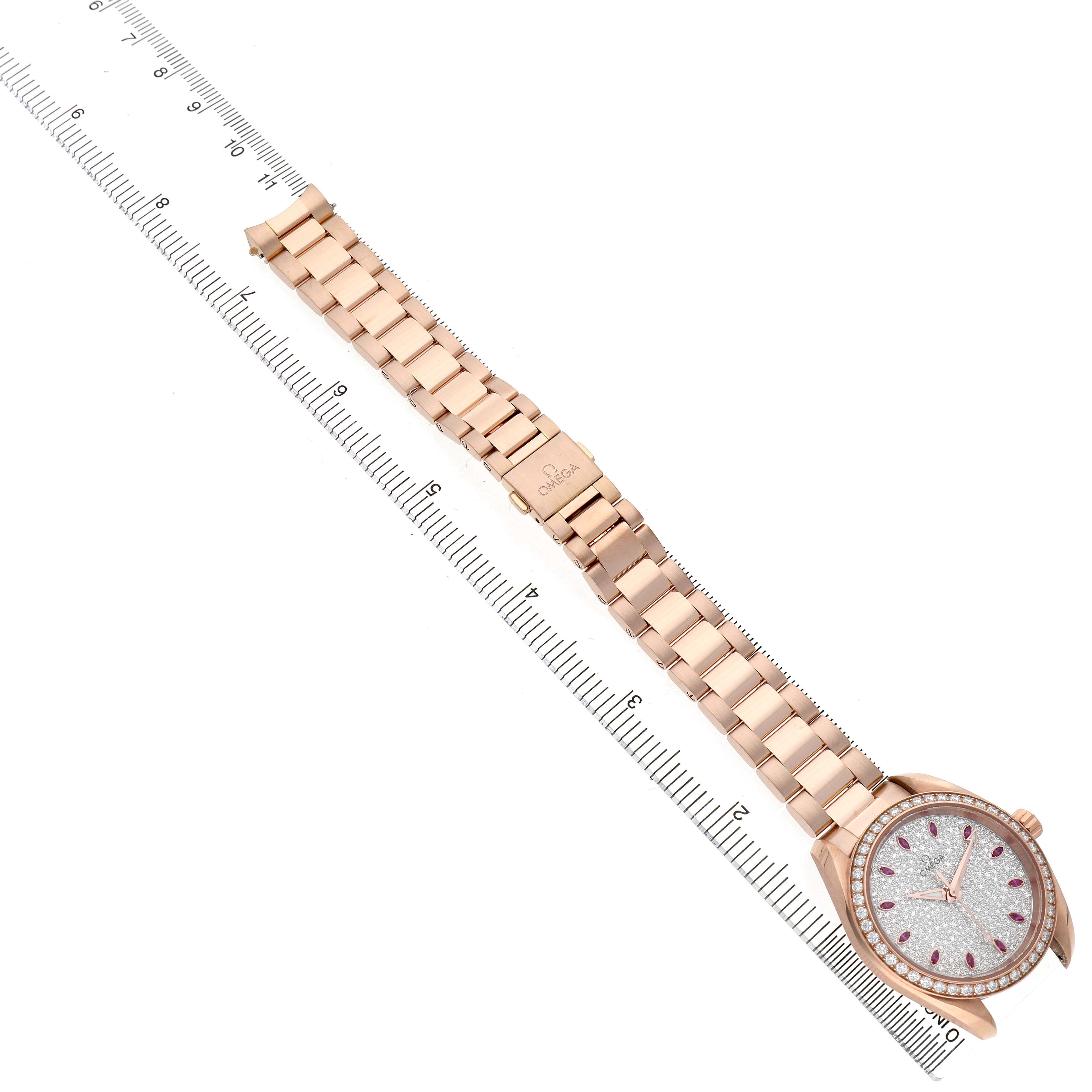 The Omega 220.55.34.20.99.001 Women's Rose Gold Silver Dial Aqua Terra 34 Rose Gold Diamond Ruby Ladies watch is shown from a top view, displaying the full bracelet and watch face alongside a ruler.