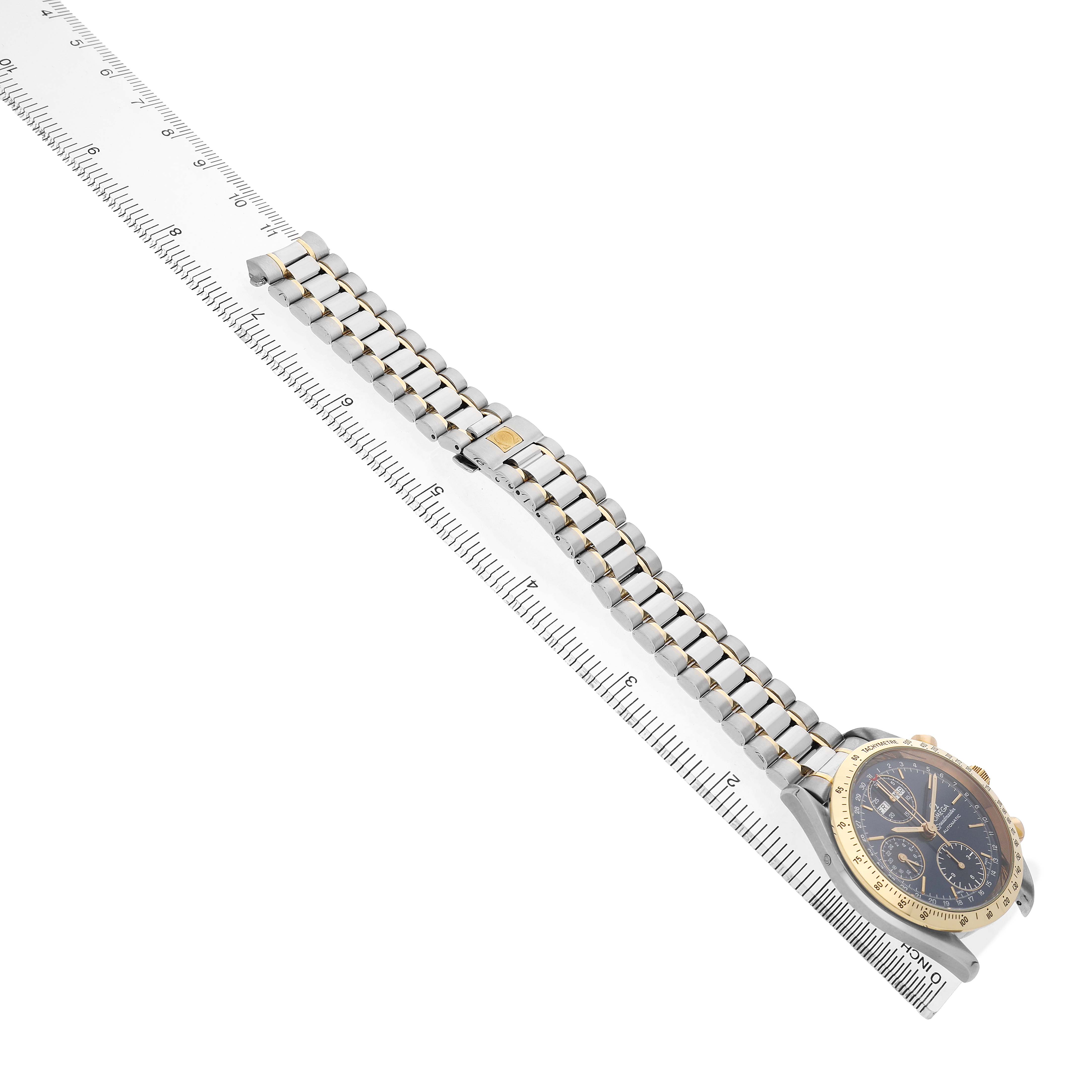 The Omega Speedmaster 3321.80.00 Men's Steel and Gold (two tone) Blue Dial watch is shown from a side angle, highlighting the bracelet and case against a ruler.