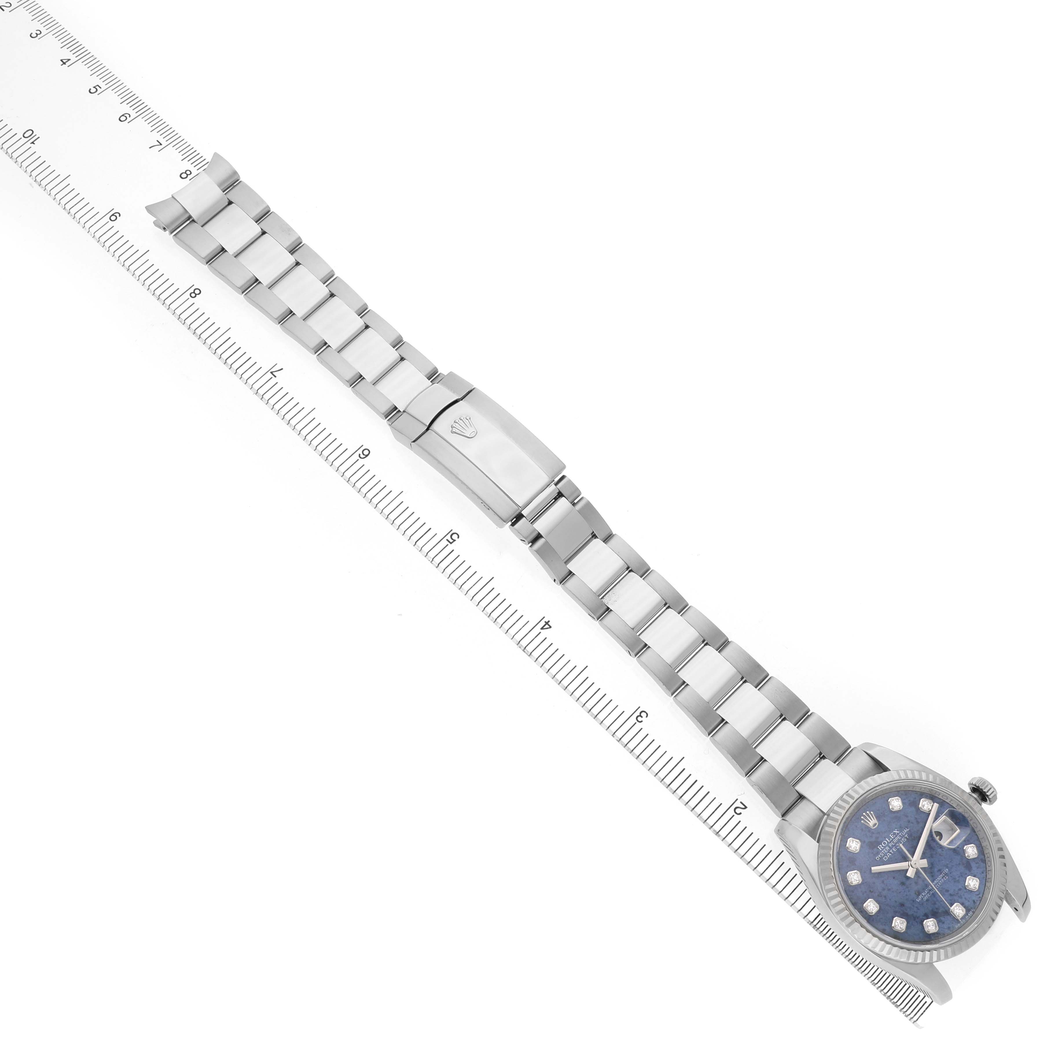 The image shows a Rolex Datejust 116234 Men's Stainless Steel Blue Dial watch from a top-down angle, highlighting the face, bracelet, and clasp alongside a ruler for scale.