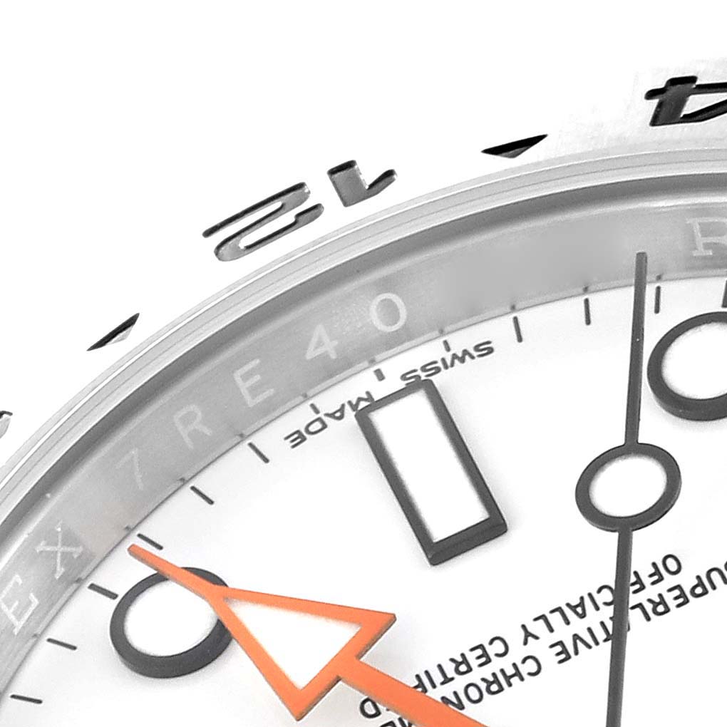 Close-up of a Rolex Explorer 216570 Men's Stainless Steel White Dial 216570 Men's Stainless Steel White Dial watch showing part of the bezel, dial, indices, and the orange arrow hand.