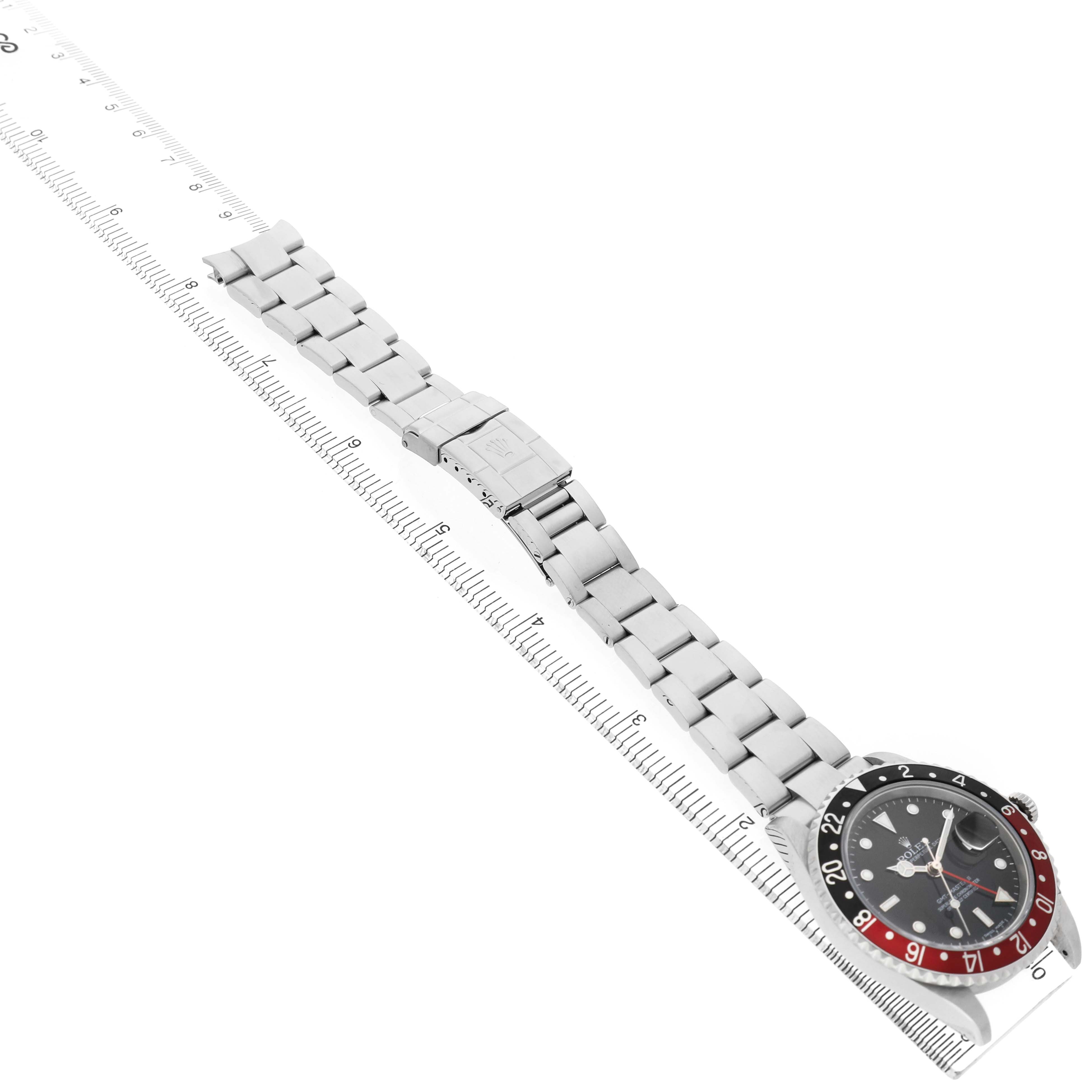 The Rolex GMT-Master 16710 Men's Stainless Steel Black Dial watch is shown at an oblique angle featuring the dial, bezel, and metal bracelet alongside a ruler.