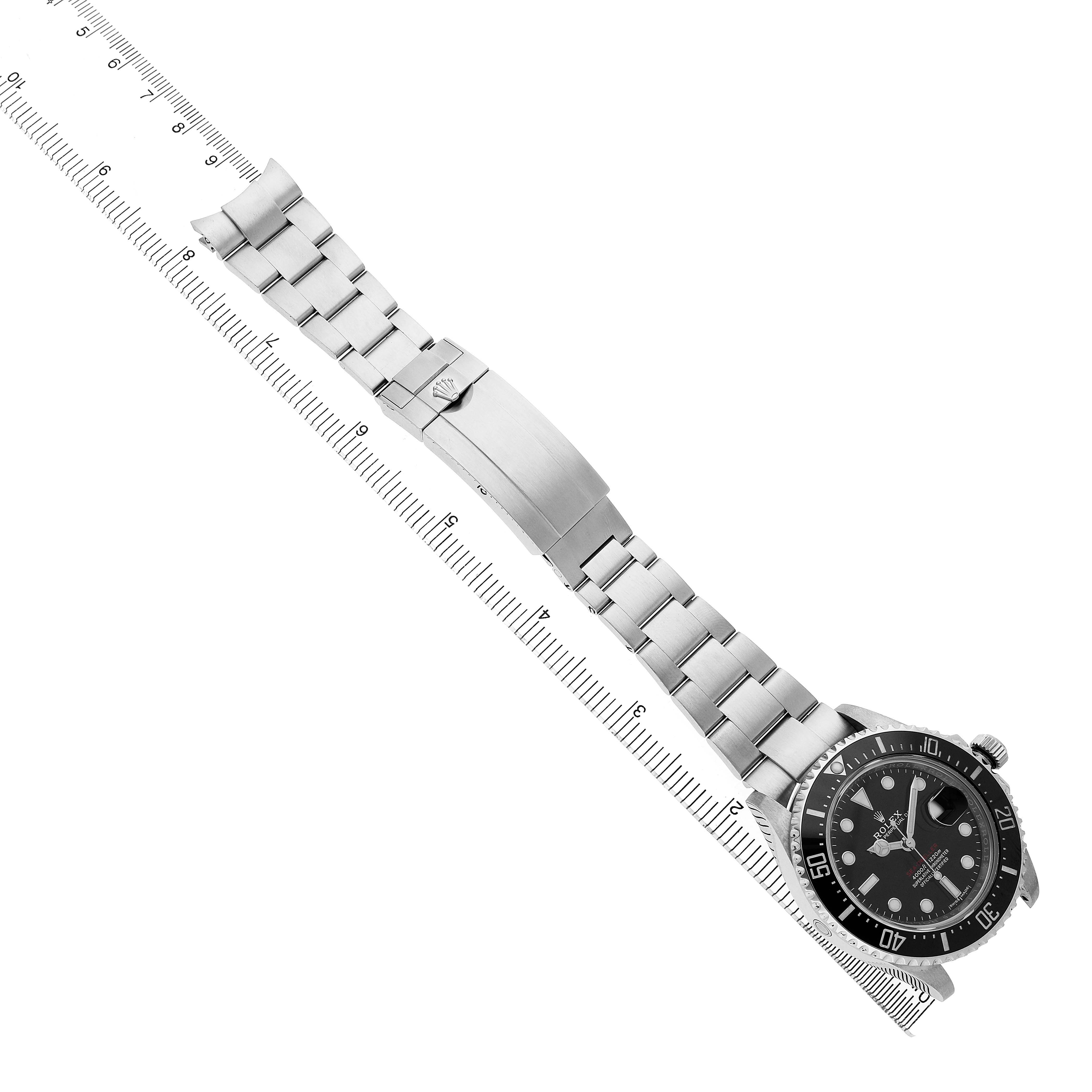 The Rolex Sea-Dweller 126600 Men's Stainless Steel Black Dial watch is shown from an overhead angle, displaying the full bracelet, clasp, and watch face alongside a ruler.