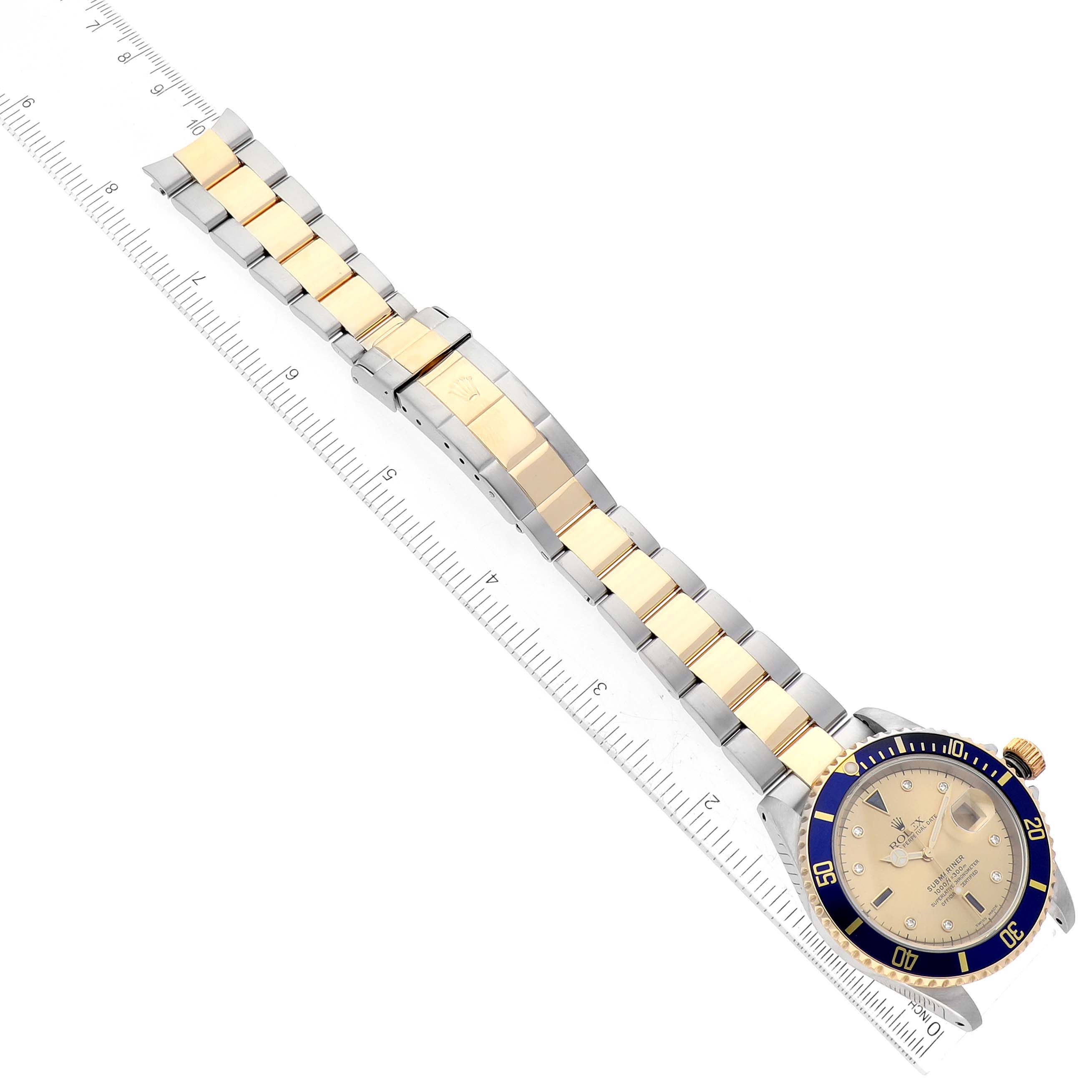 This image shows a Rolex Submariner 16613 Men's Steel and Gold (two tone) Champagne Dial 16613 Men's Steel and Gold (two tone) Champagne Dial watch with a two-tone bracelet, placed next to a ruler for scale.