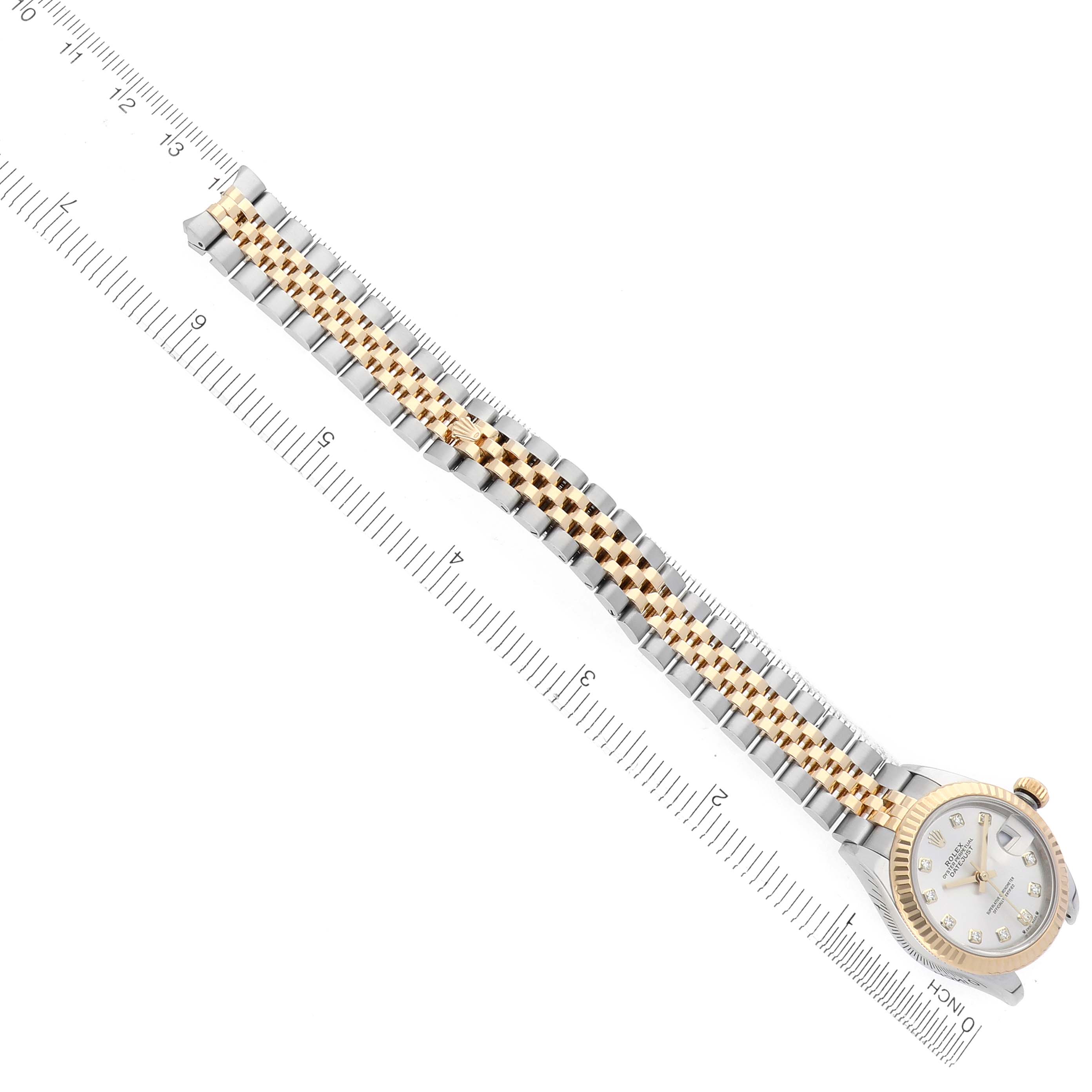 The Rolex Datejust watch is shown from a top angle with the face, bracelet, and clasp visible alongside a ruler.