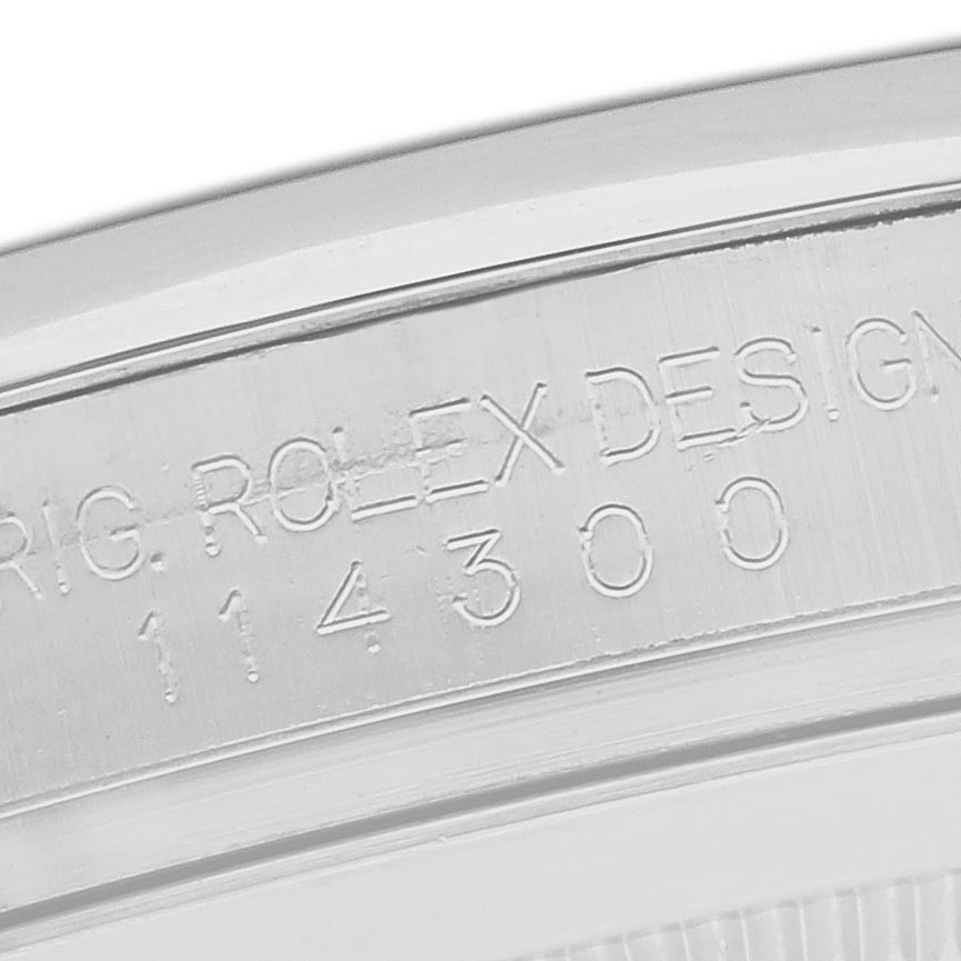 The image shows an angled close-up of the case back edge with engravings on the Rolex Oyster Perpetual 114300 Men's Stainless Steel Blue Dial 114300 Men's Stainless Steel Blue Dial.
