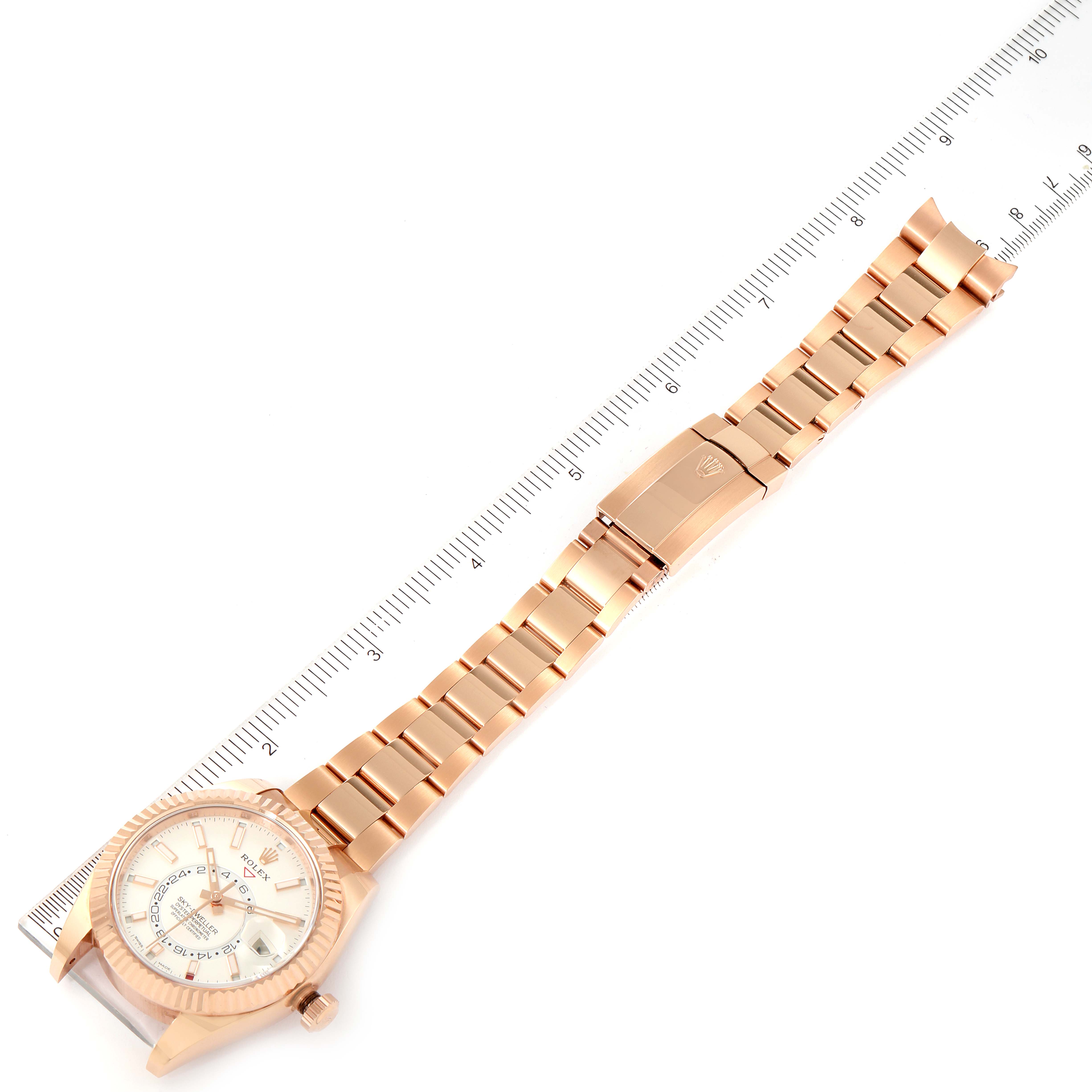 The image shows an overhead view of a Rolex Sky-Dweller 326935 Men's Rose Gold White Dial 326935 Men's Rose Gold White Dial watch laid flat alongside a ruler.