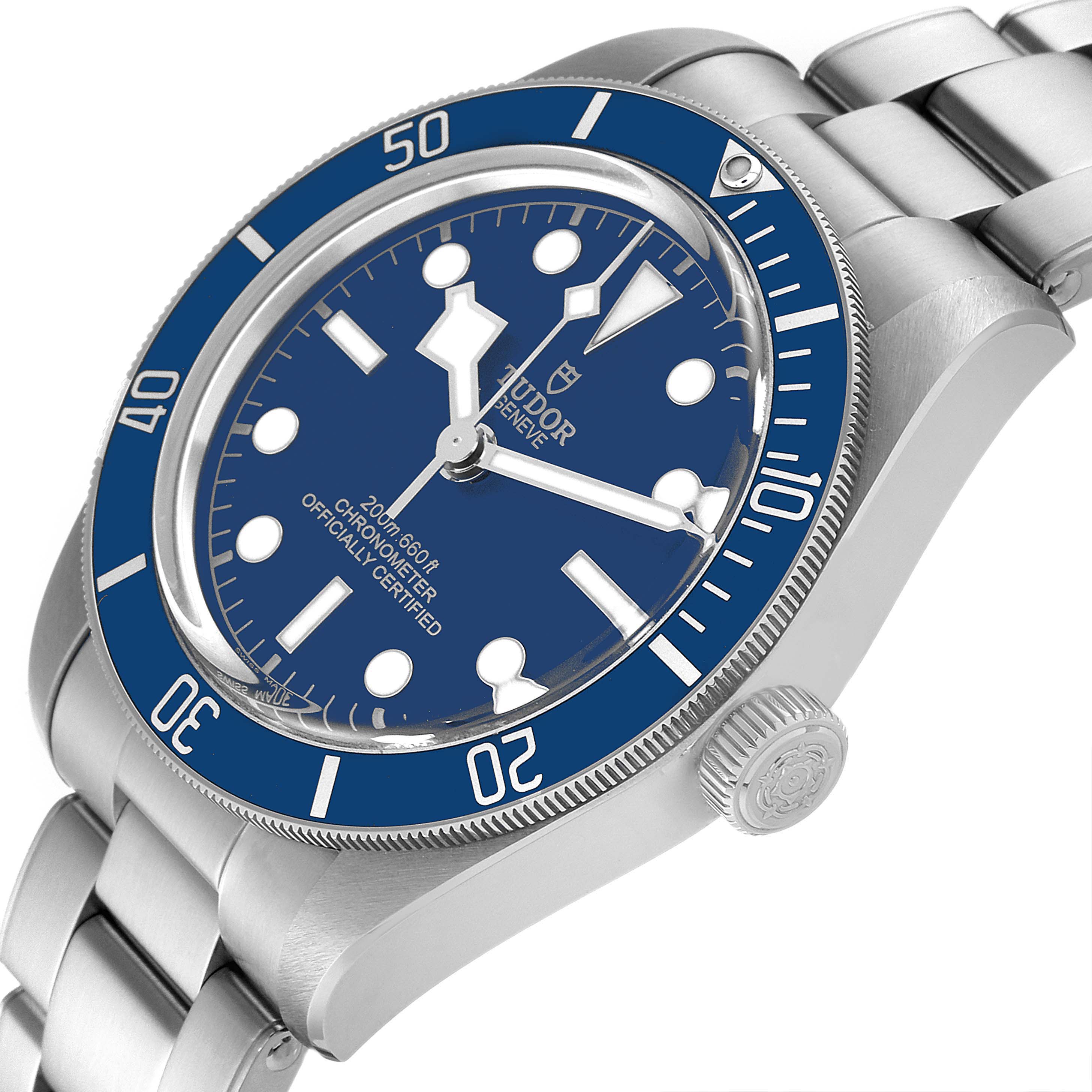 The Heritage Black Bay by Tudor is shown at an angled side view, highlighting the blue bezel, dial, and stainless steel bracelet.