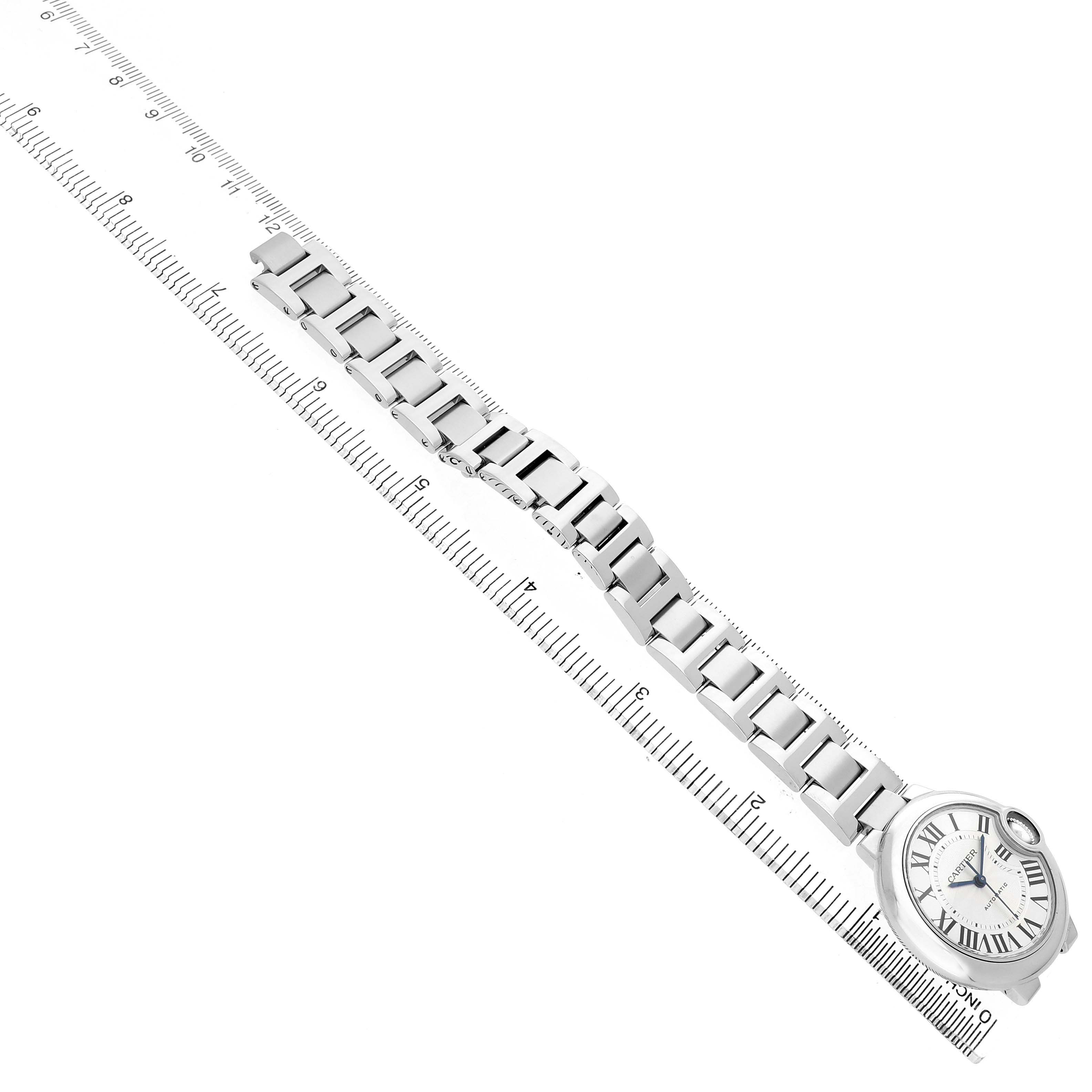 The Cartier Ballon Bleu W6920071 Women's Stainless Steel Silver Dial watch is shown diagonally with a clear view of the face and the entire metal bracelet on a ruler.