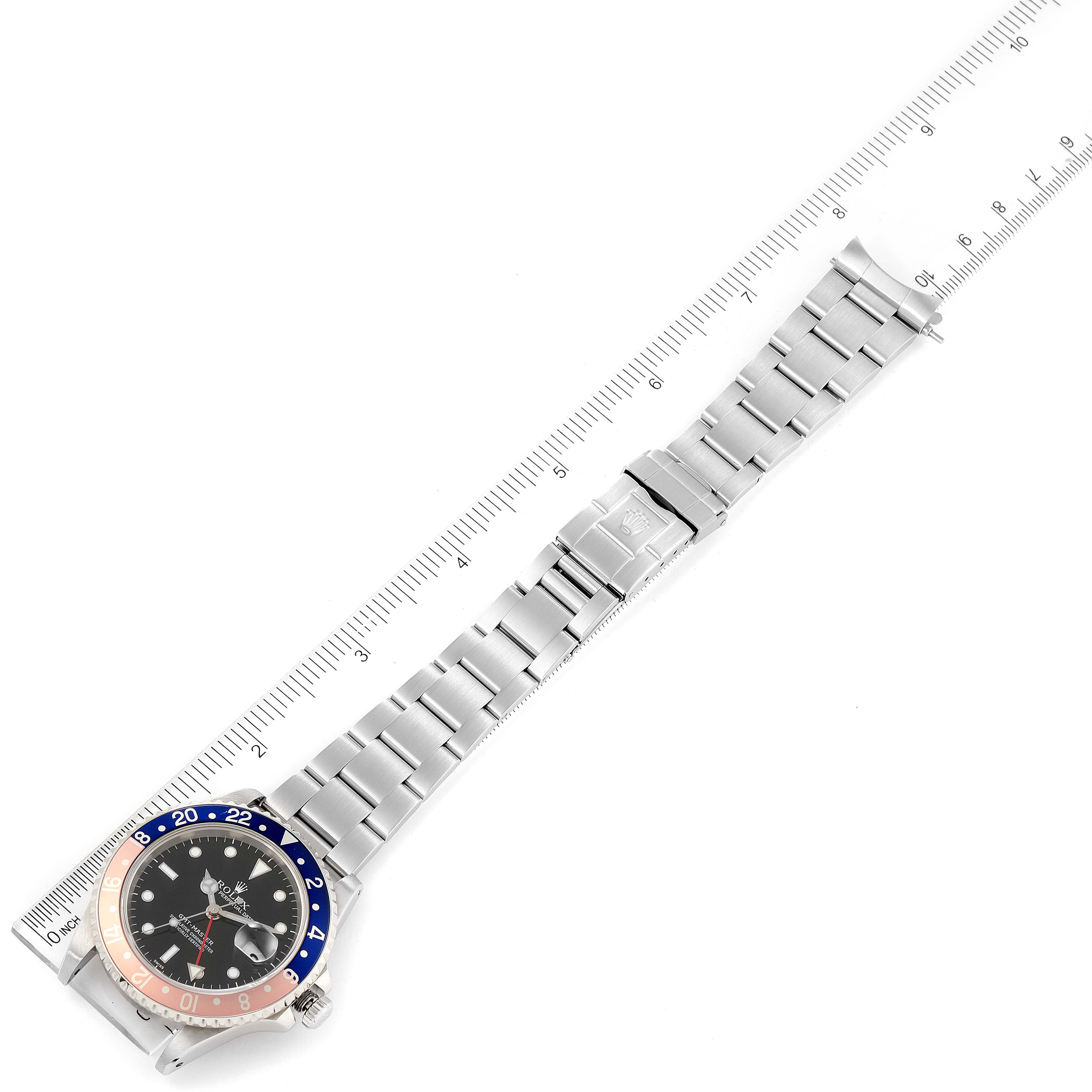 The image shows an overhead view of a Rolex GMT-Master 16700 Men
s Stainless Steel Black Dial 16700 Men
s Stainless Steel Black Dial watch with a ruler beside it, highlighting the watch band and face.