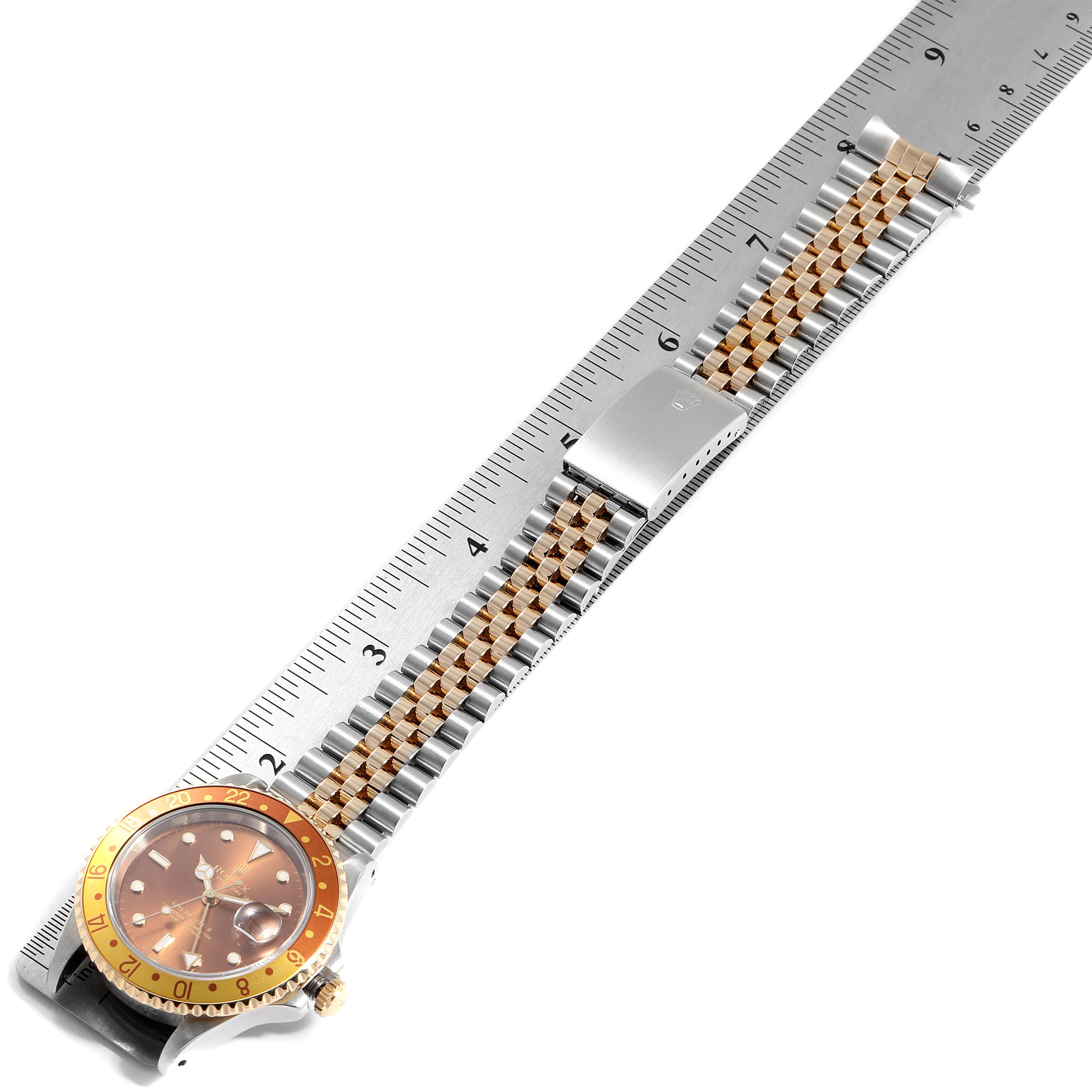 The image shows a Rolex GMT-Master 16713 Men's Steel and Gold (two tone) Brown Dial 16713 Men's Steel and Gold (two tone) Brown Dial watch laid flat with a two-tone bracelet and bezel, next to a ruler.