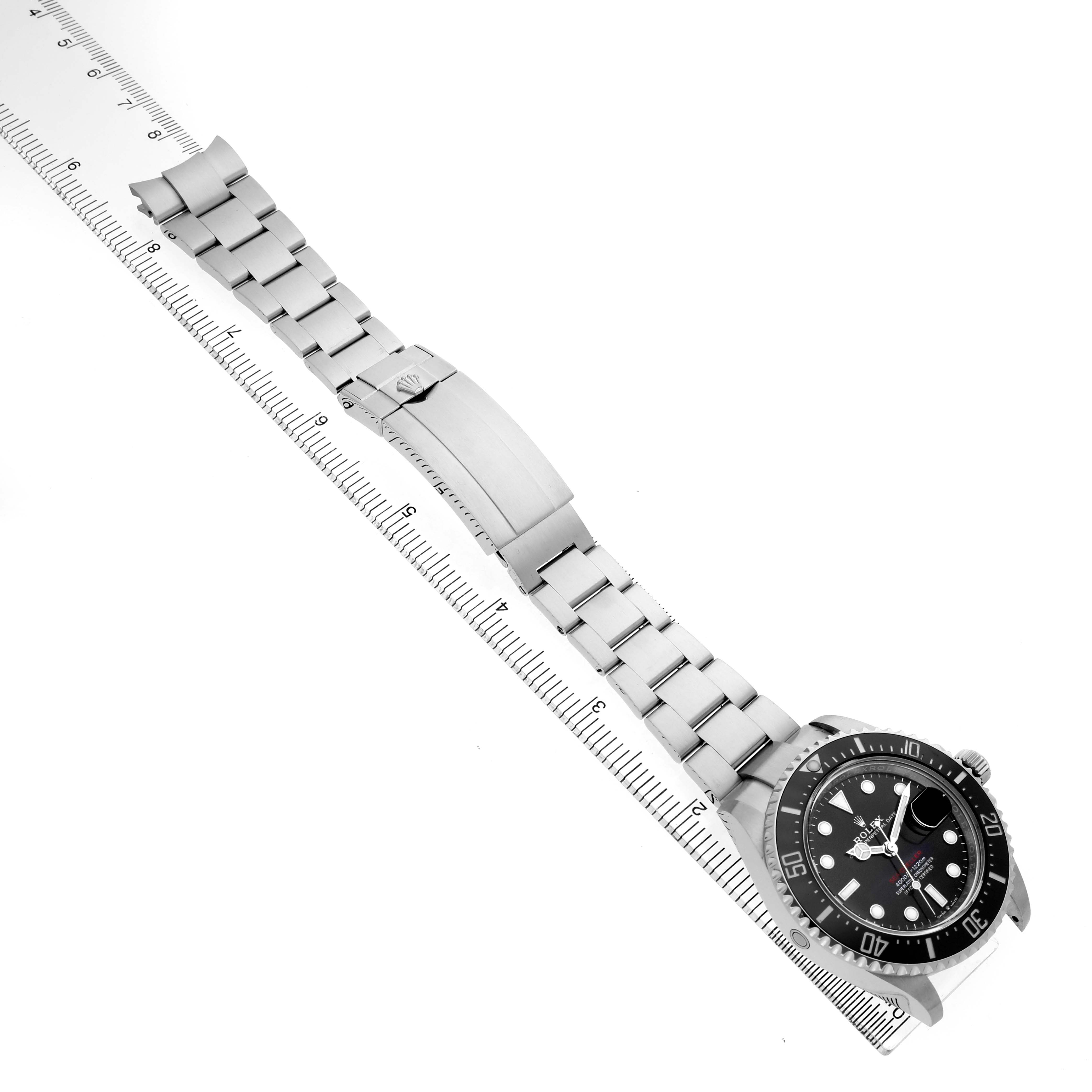 The image shows a side view of a Rolex Sea-Dweller 126600 Men's Stainless Steel Black Dial watch with its bracelet and clasp fully extended alongside a ruler.