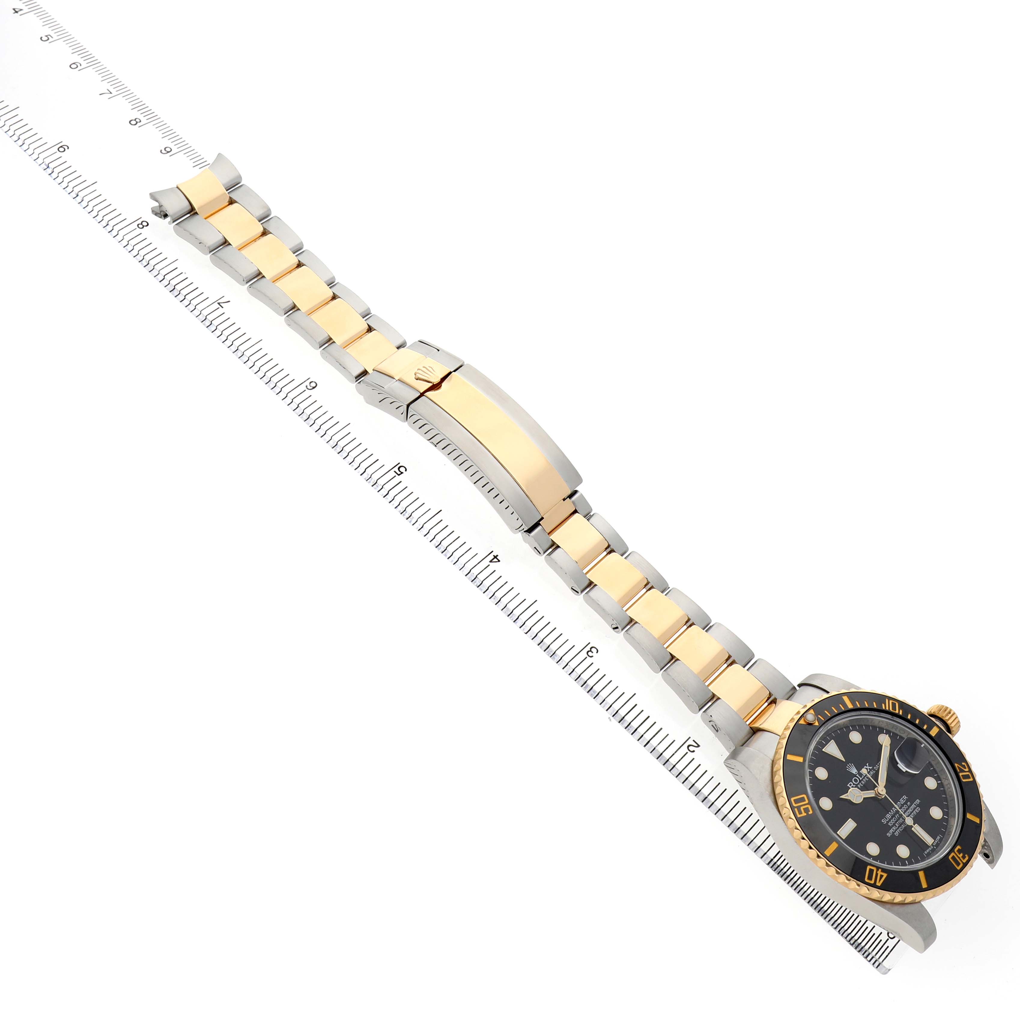 The Rolex Submariner 116613 Men's Steel and Gold (two tone) Black Dial watch is shown from the side, highlighting the bracelet, clasp, and face, aligned next to a ruler.
