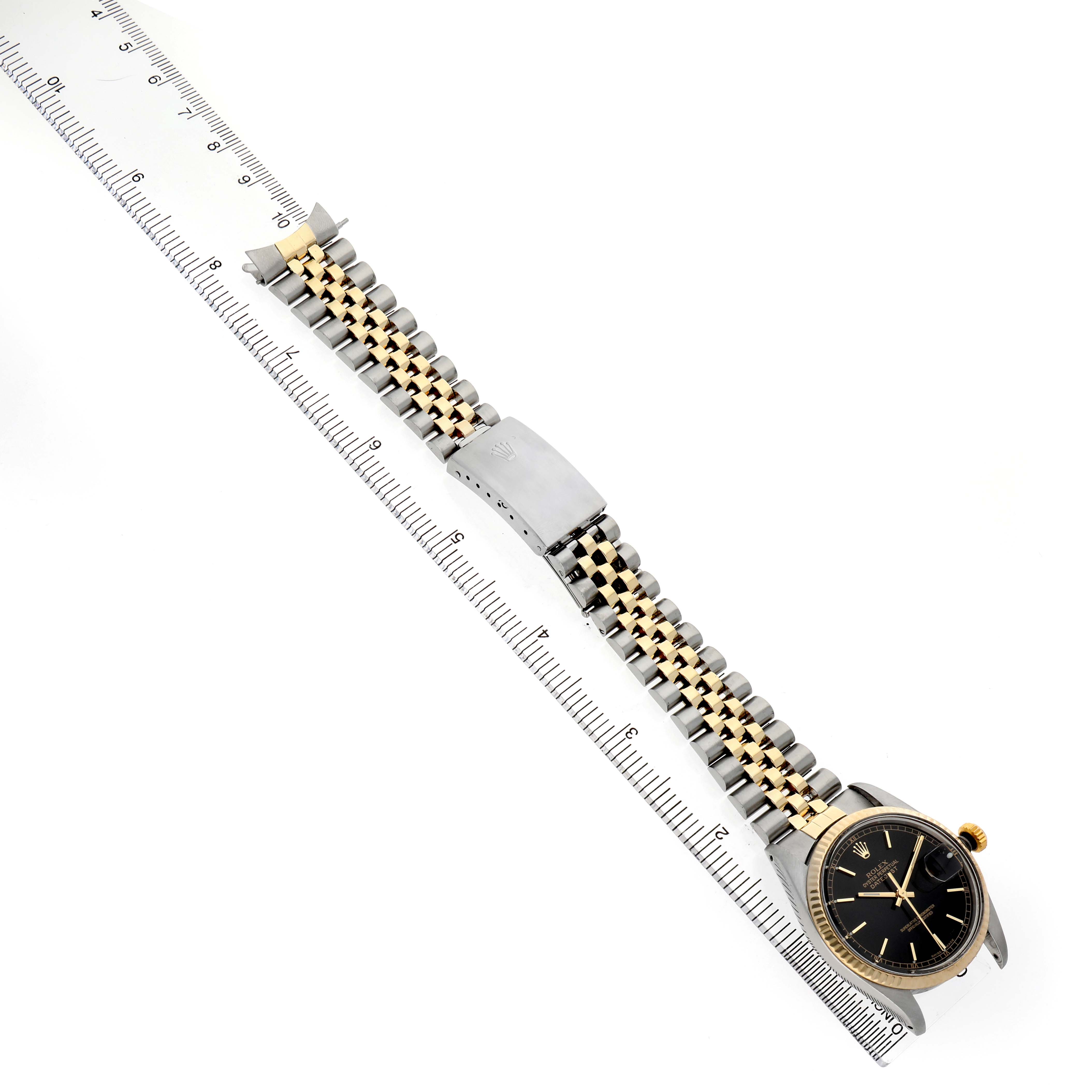 The Rolex Datejust 16013 Men's Steel and Gold (two tone) Black Dial watch is shown from an angled top view, featuring the bracelet, clasp, and case near a ruler for scale.