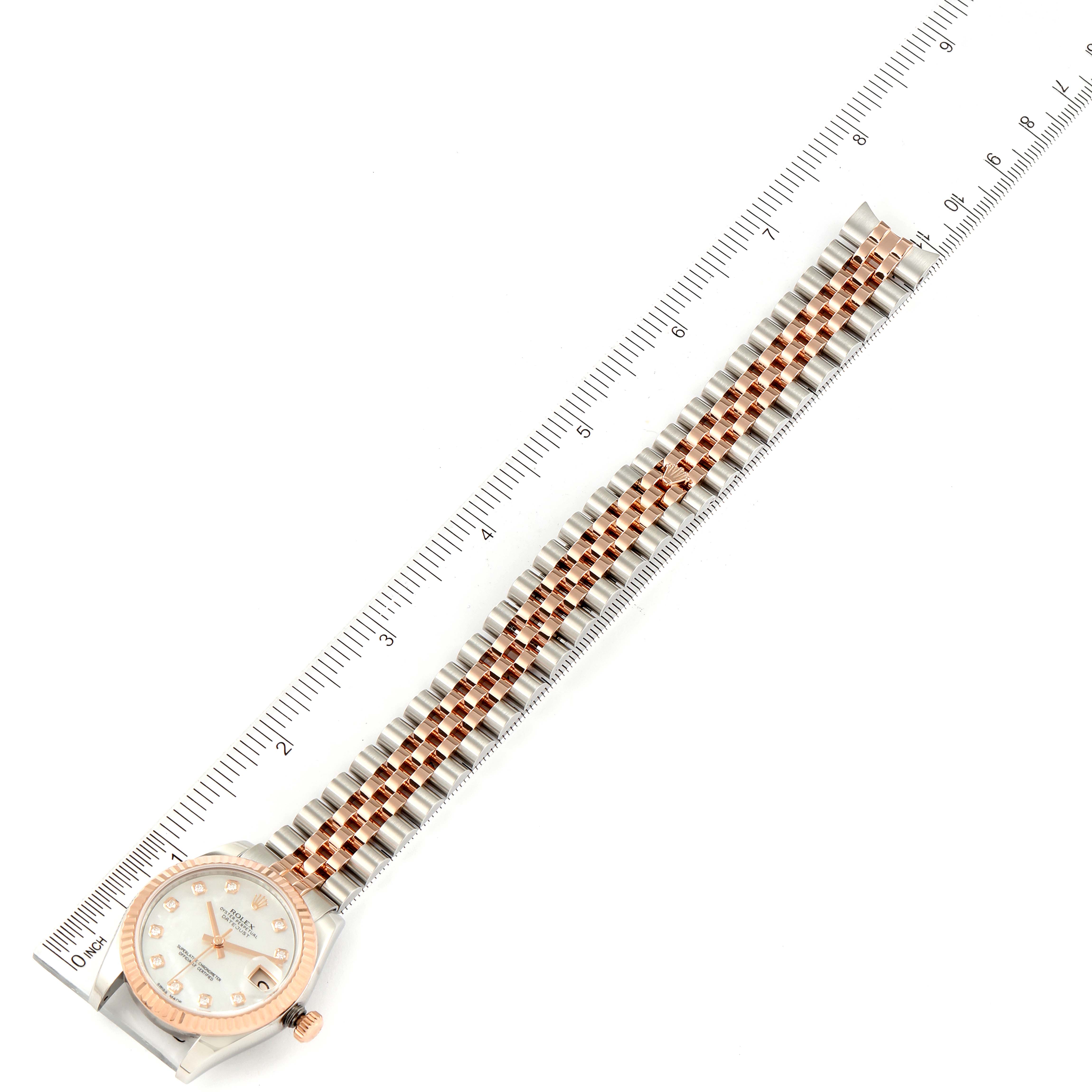 The image shows a Mid-Size Rolex watch lying flat with a ruler beside it, displaying the full face and bracelet.