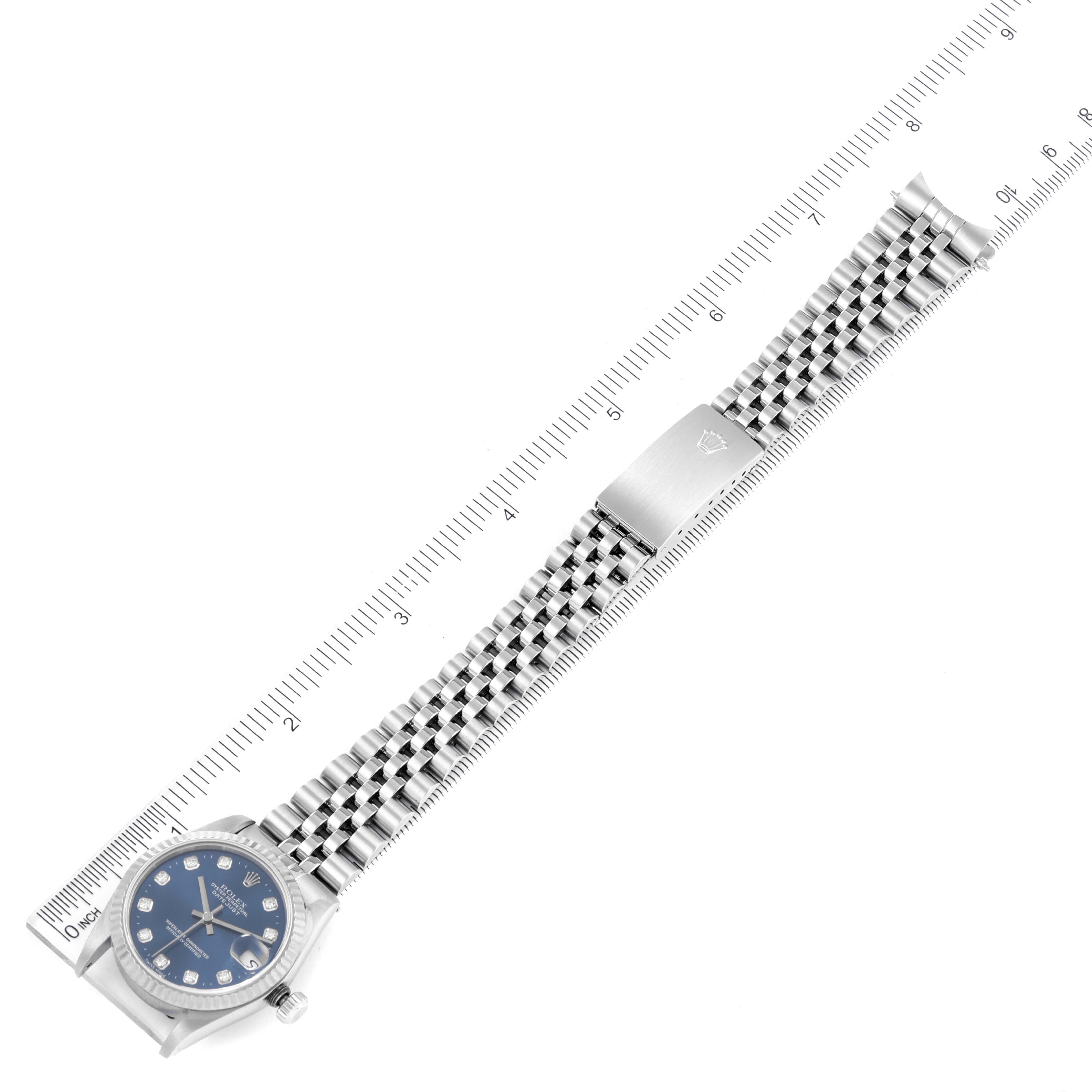 The image shows a top-down view of a Mid-Size Rolex watch with a blue dial, metal bracelet, and an integrated clasp, alongside a ruler.