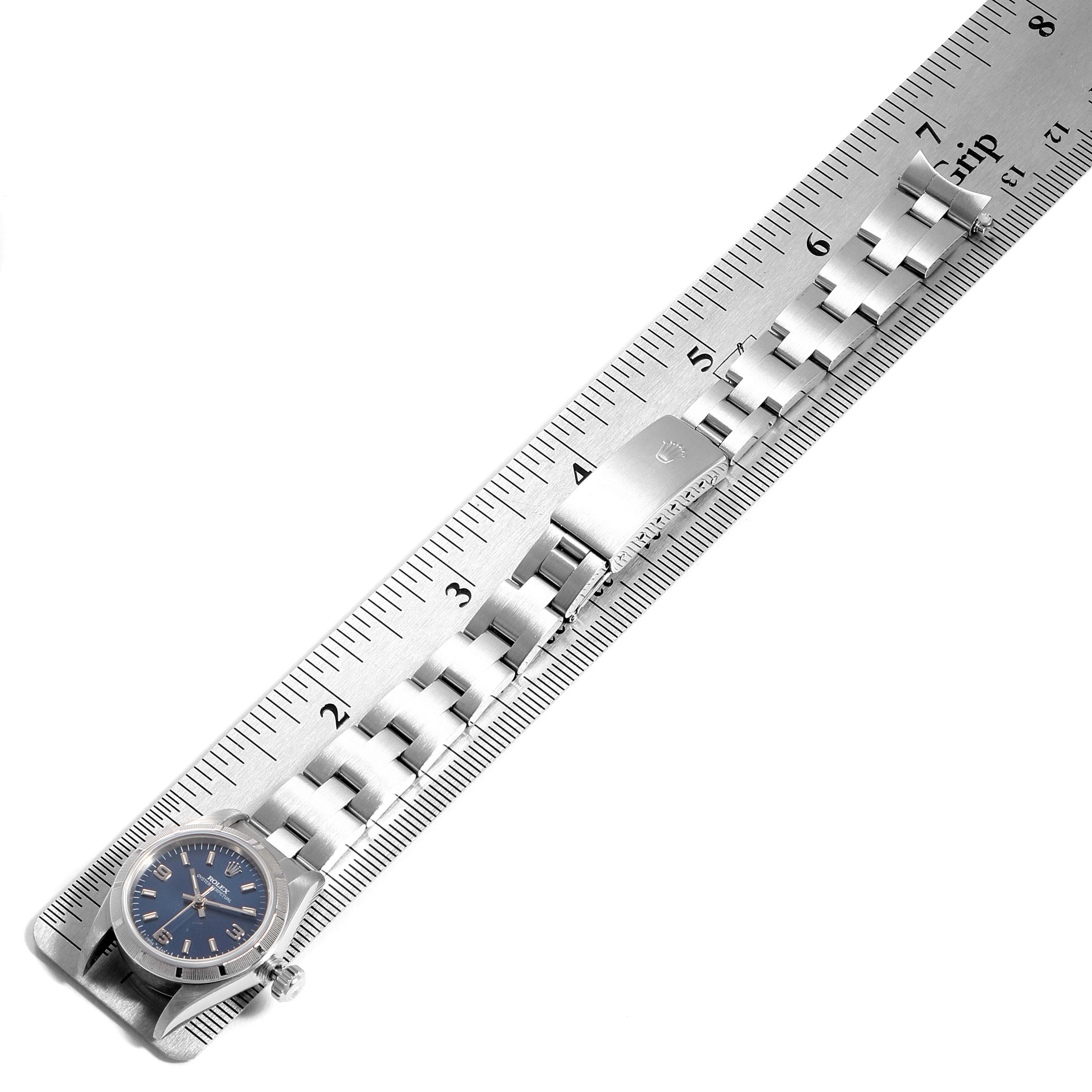 The image shows a Rolex Oyster Perpetual 67230 Women
s Stainless Steel Blue Dial 67230 Women
s Stainless Steel Blue Dial watch at an overhead angle, focusing on the face, band, and clasp aligned with a ruler.