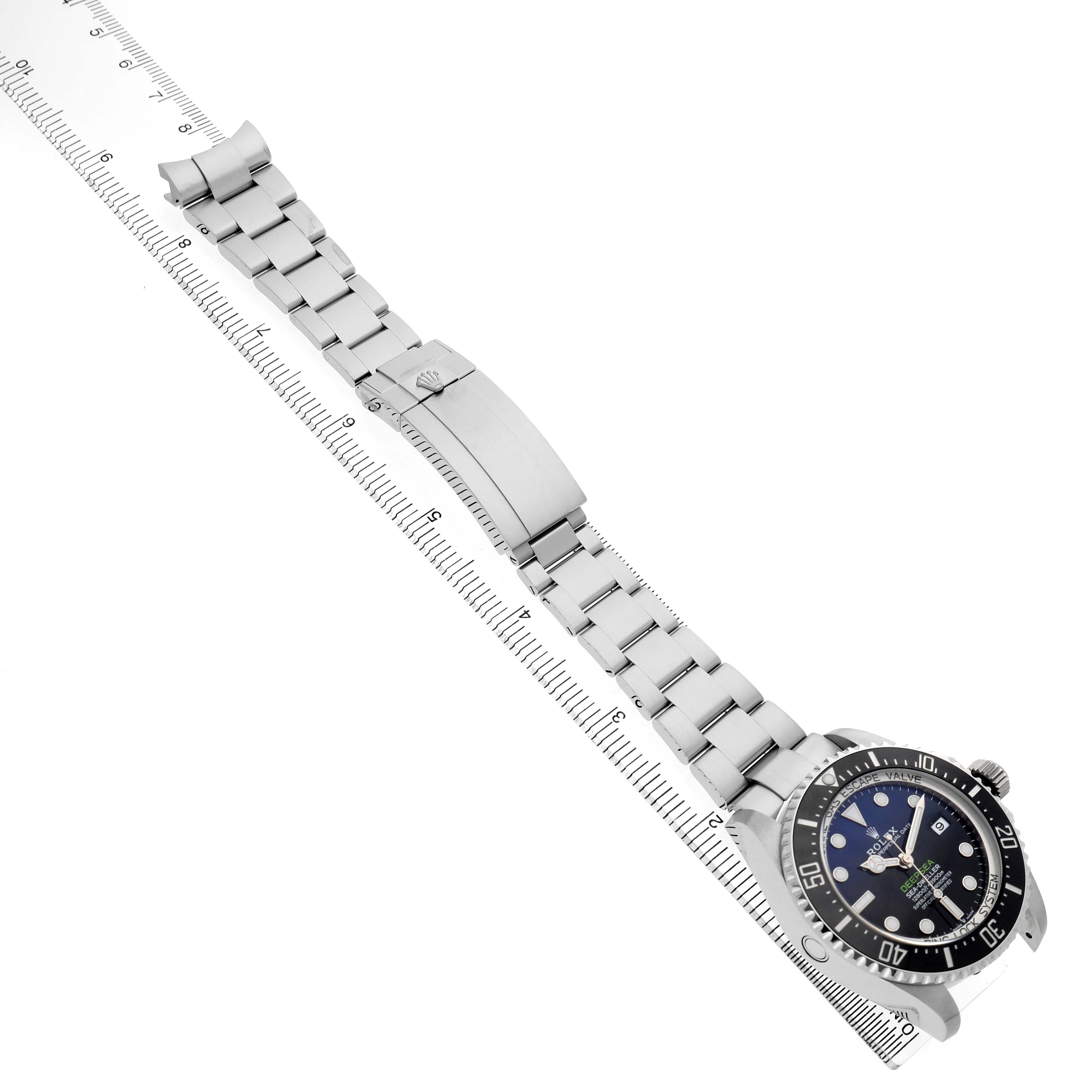 The Rolex Sea-Dweller 136660 Men's Stainless Steel Blue Dial watch is shown at an angle, displaying the face, bezel, bracelet, and deployment clasp with a ruler for scale.