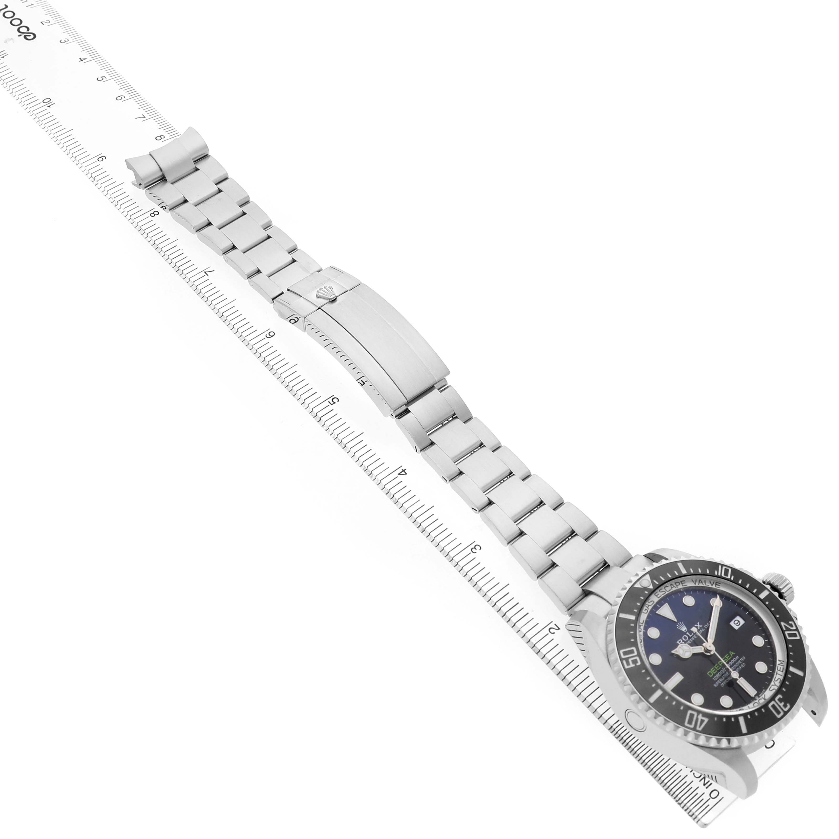 The Rolex Sea-Dweller 136660 Men's Stainless Steel Blue Dial is displayed diagonally, showcasing the dial, bezel, bracelet, and clasp against a ruler.