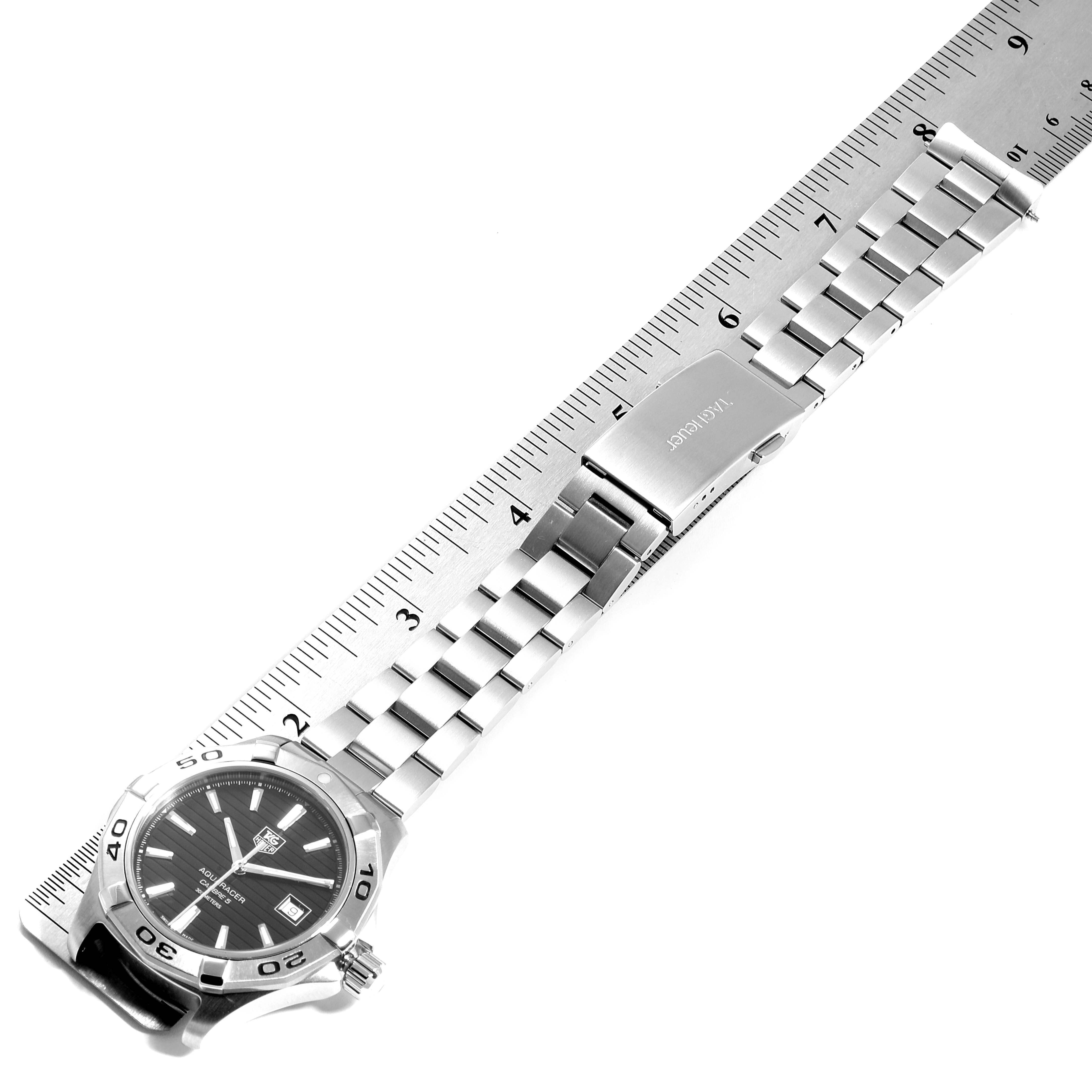 This image shows a Tag Heuer Aquaracer WAY2110.BA0928 Men
s Stainless Steel Black Dial WAY2110.BA0928 Men
s Stainless Steel Black Dial watch laid flat next to a ruler, highlighting its bracelet and clasp.