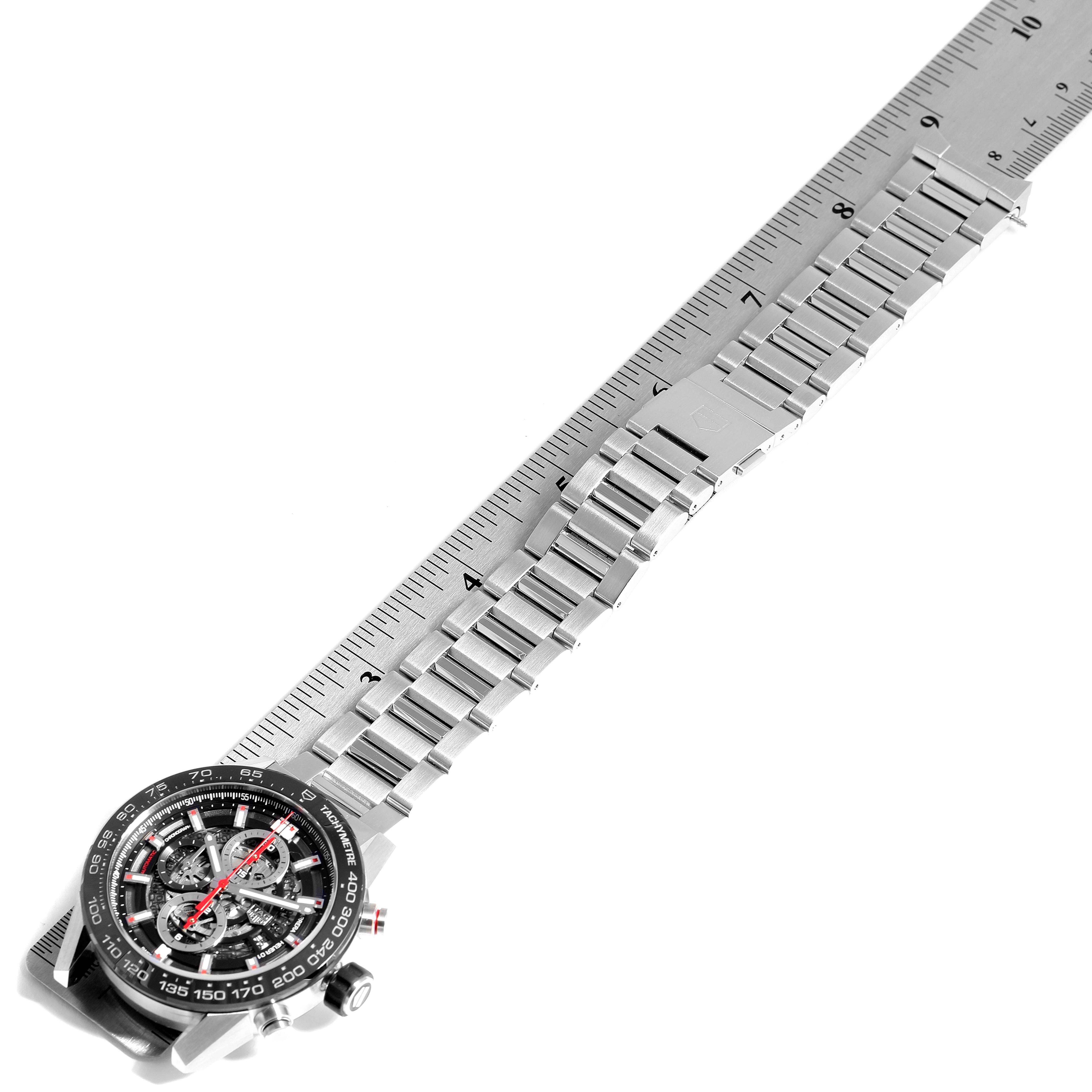 The image shows a Tag Heuer Carrera CAR2A1W.BA0703 Men's Stainless Steel Transparent Dial CAR2A1W.BA0703 Men's Stainless Steel Transparent Dial watch viewed from the top, highlighting the face and metallic bracelet laid out straight next to a ruler.
