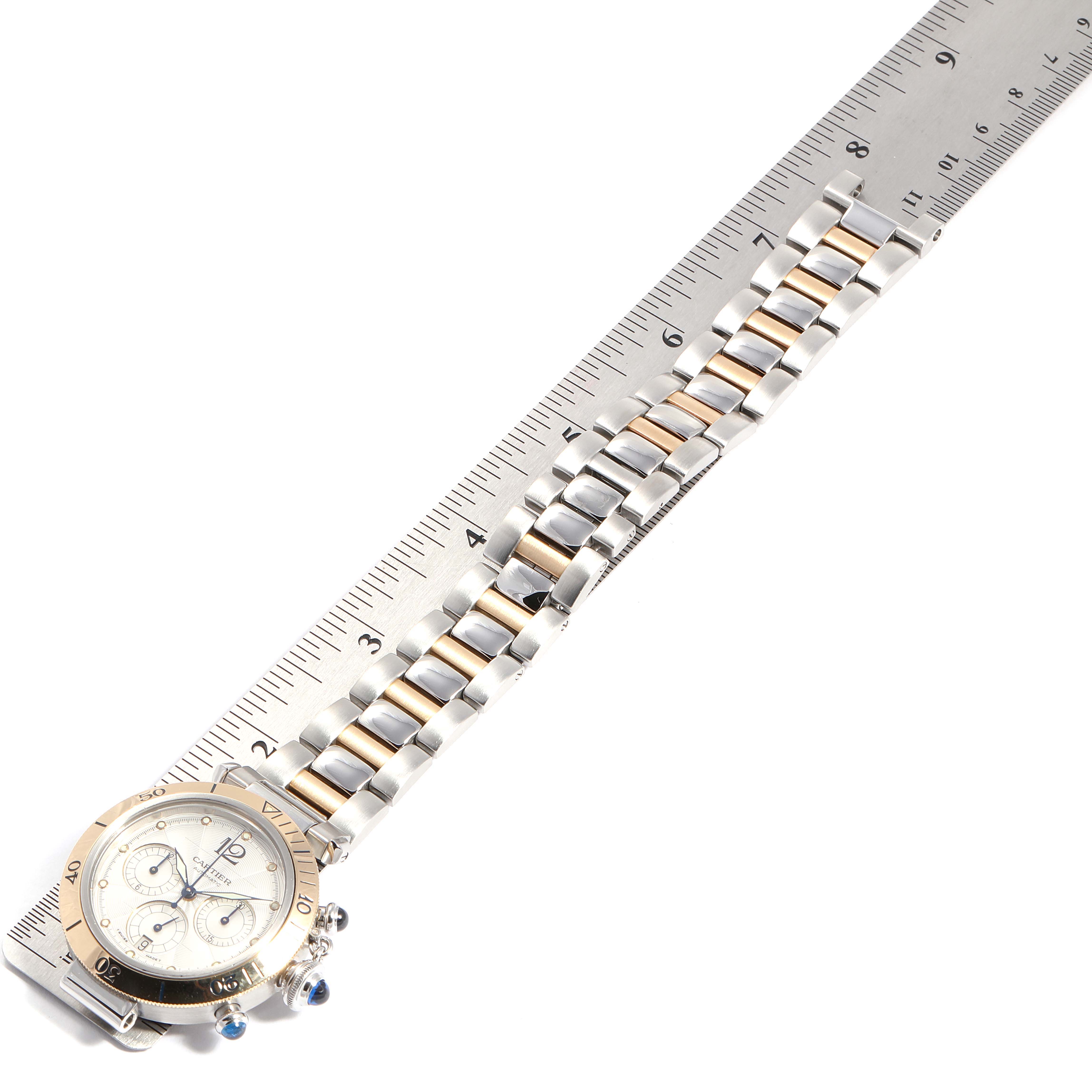 The image shows a Cartier Pasha W31036T6 Men's Steel and Gold (two tone) Silver Dial W31036T6 Men's Steel and Gold (two tone) Silver Dial watch laid flat on a ruler, highlighting the face and the metal bracelet.