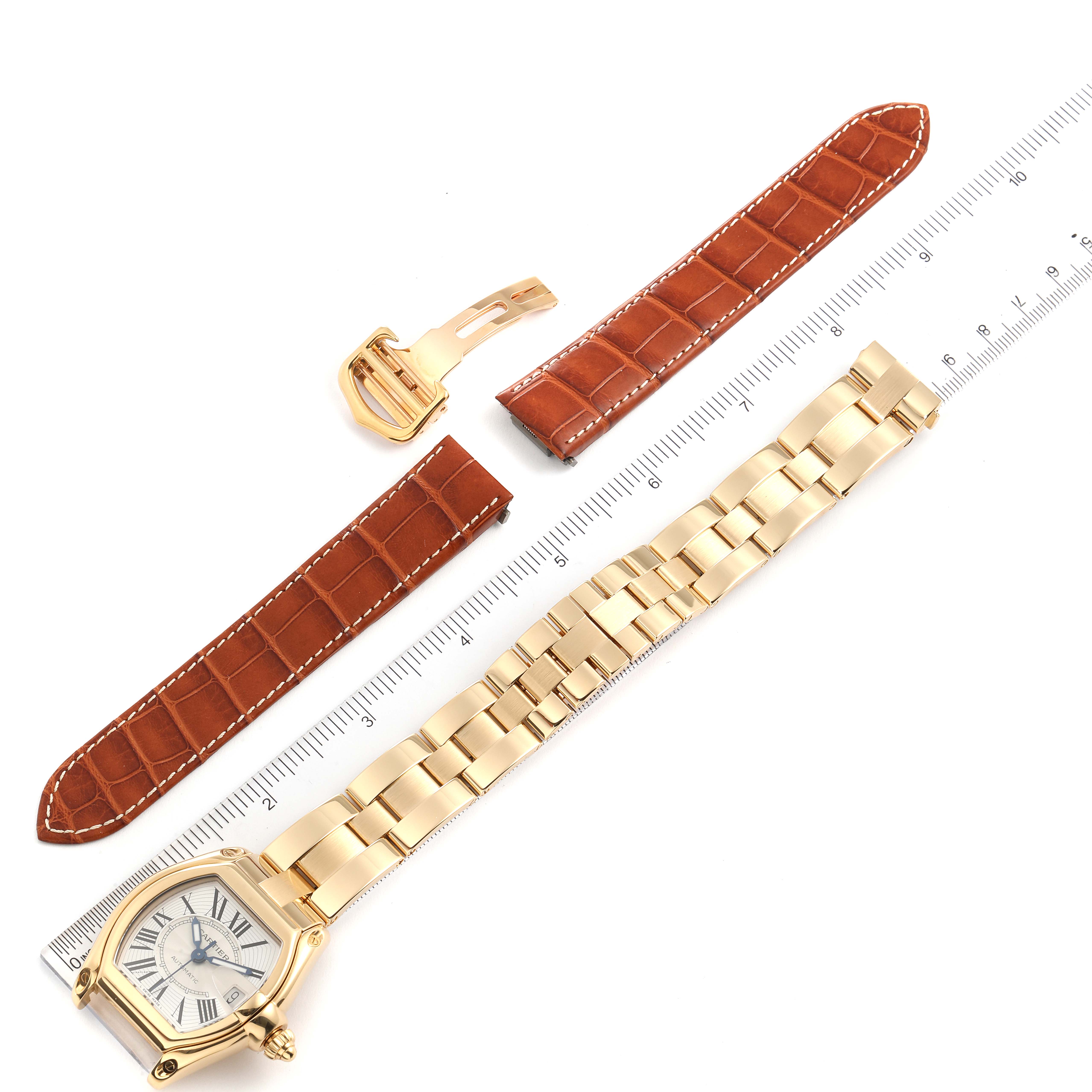 This image shows a Cartier Roadster W62005V1 Men's Yellow Gold Silver Dial W62005V1 Men's Yellow Gold Silver Dial watch laid flat alongside a measuring ruler with additional leather watch straps and a buckle.