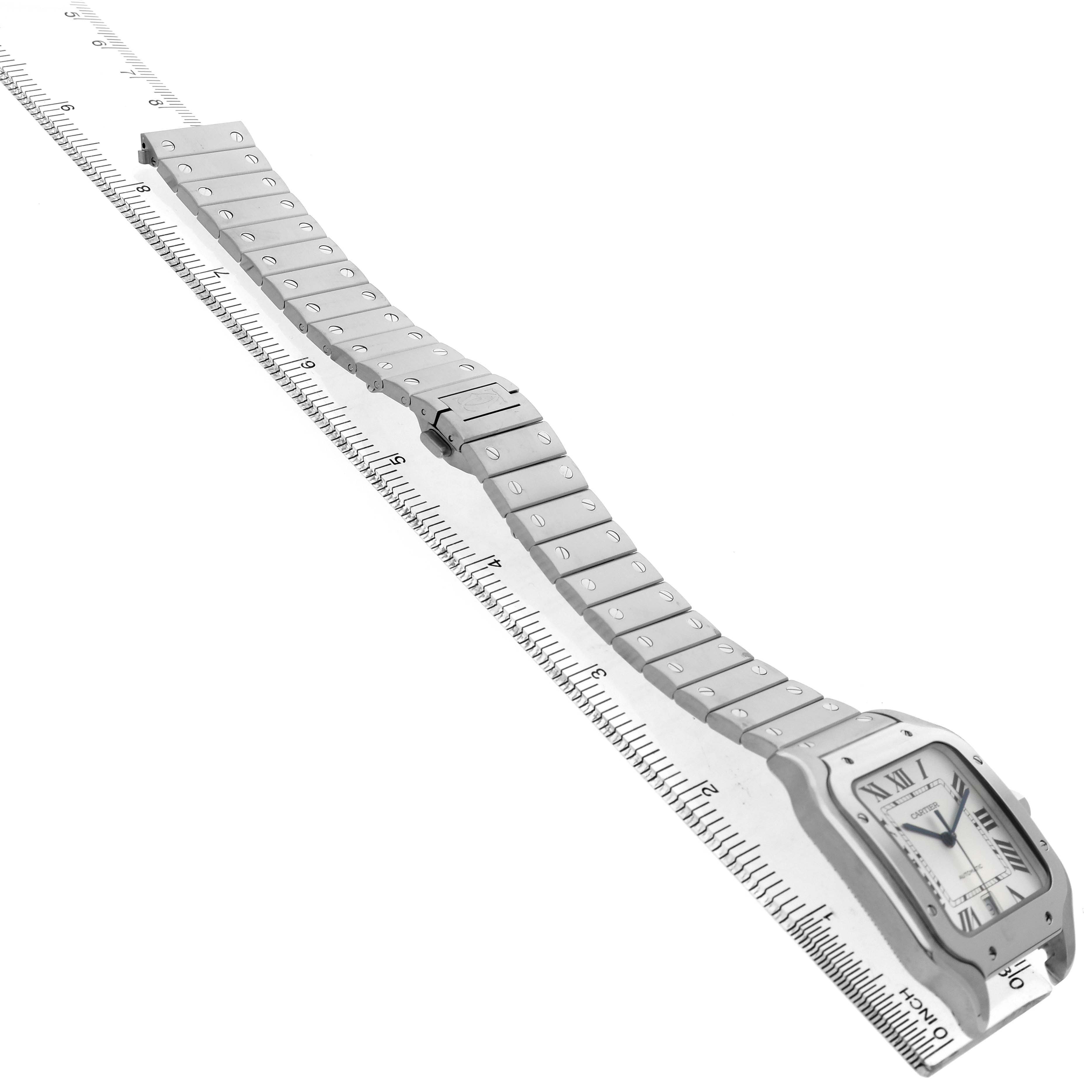 The Cartier Santos WSSA0009 Men's Stainless Steel Silver Dial watch is shown at an angle highlighting the face and entire linked bracelet, laid over a ruler.