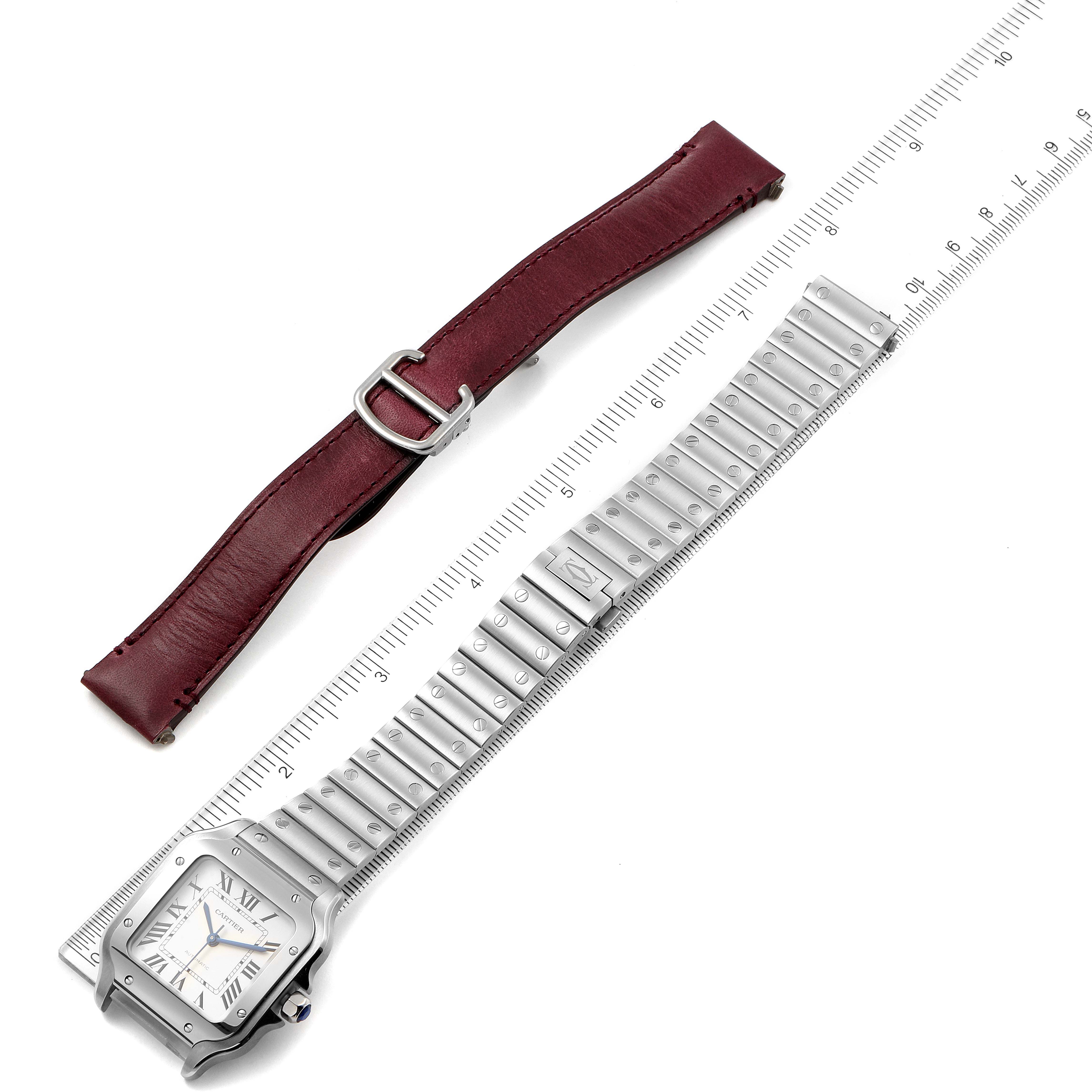 The image shows a Cartier Santos WSSA0029 Men's Stainless Steel Silver Dial WSSA0029 Men's Stainless Steel Silver Dial watch face with a metal strap and a separate burgundy leather strap, displayed with a ruler.
