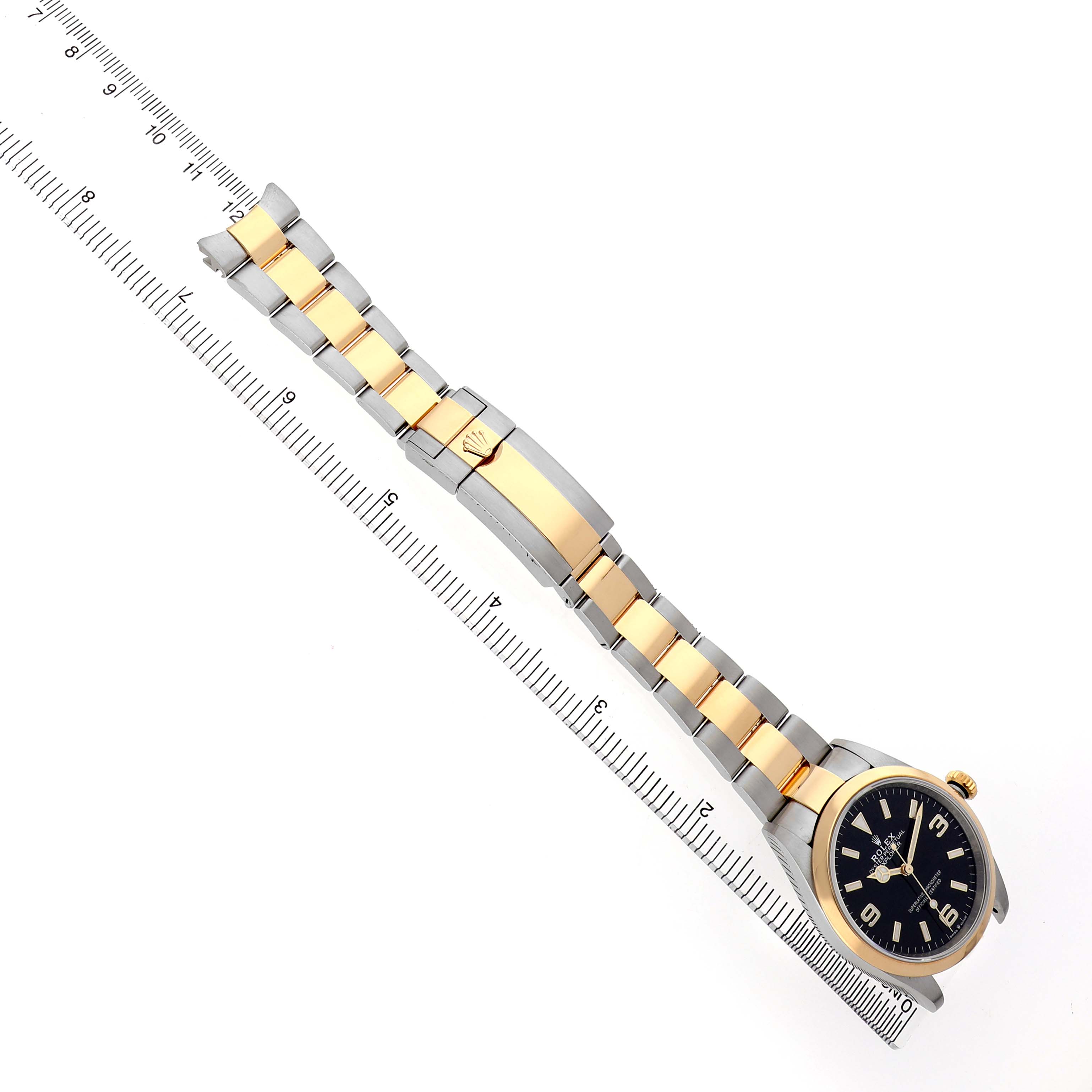 The image shows a Rolex Explorer 124273 Men's Steel and Gold (two tone) Black Dial watch laid flat with its two-tone bracelet extended alongside a ruler.