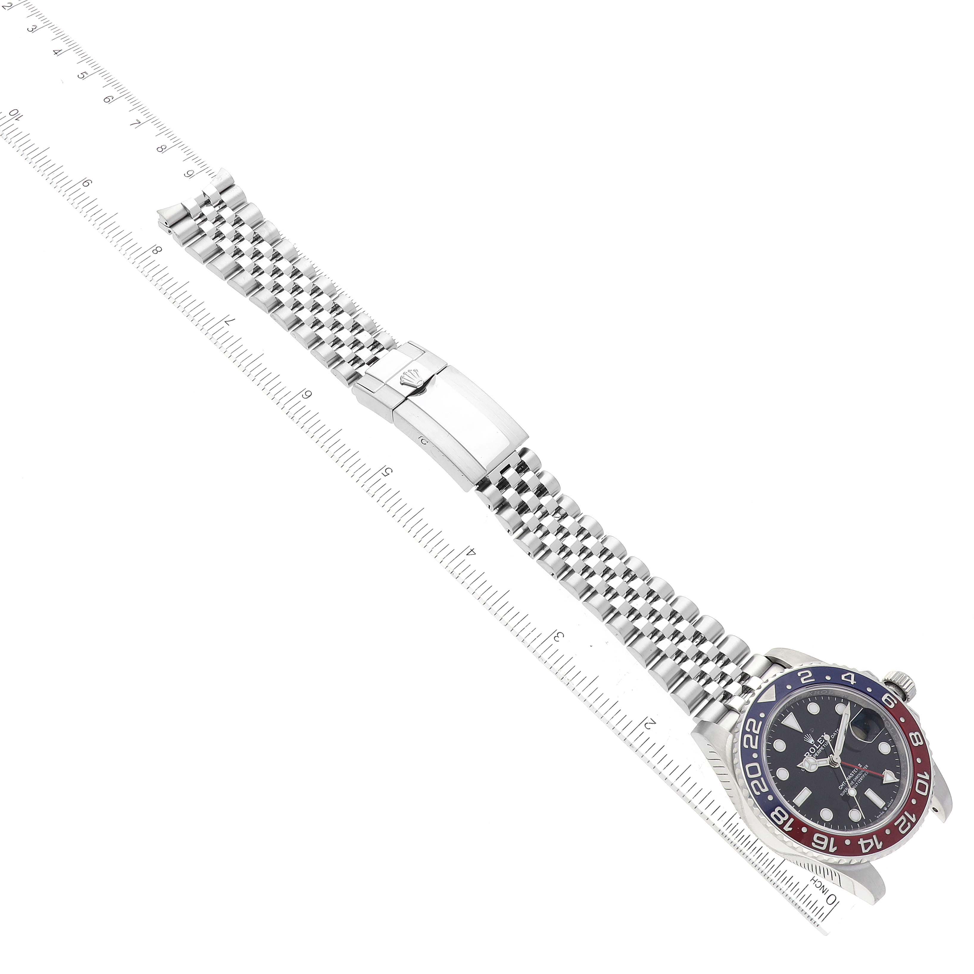 This image shows a Rolex GMT-Master 126710BLRO Men's Stainless Steel Black Dial 126710BLRO Men's Stainless Steel Black Dial watch and its metal strap, positioned alongside a ruler for measurement.