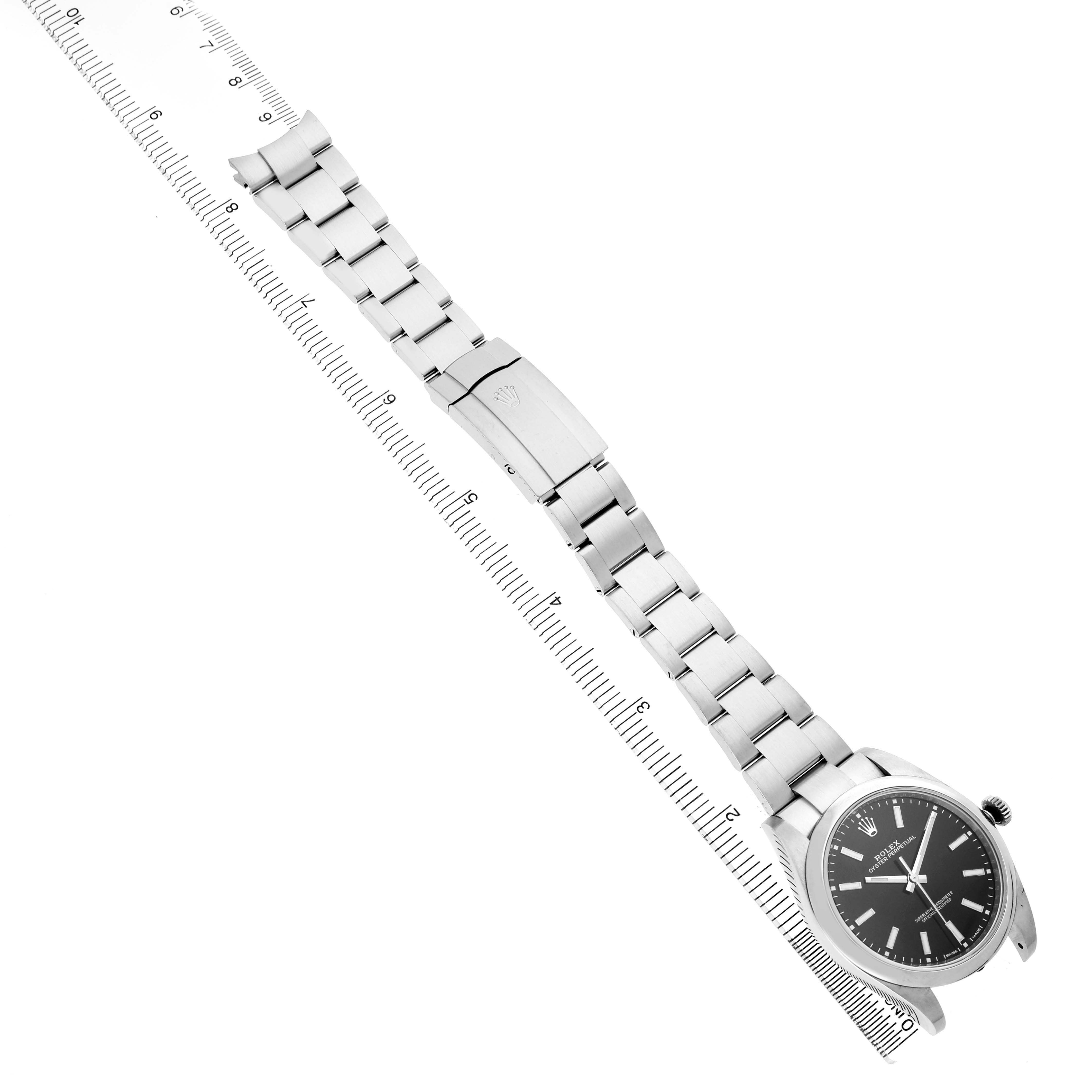 The Rolex Oyster Perpetual 114300 Men's Stainless Steel Black Dial watch is shown from a top angle, displaying the full bracelet and watch face alongside a ruler.