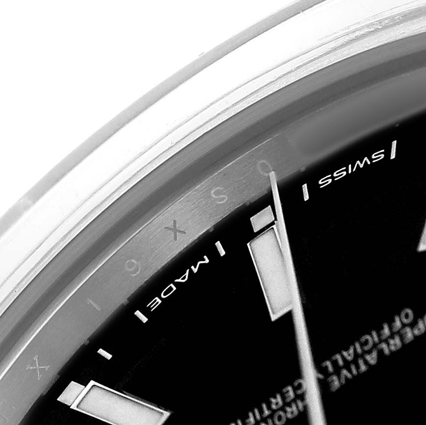 The image shows a close-up of the edge of a Rolex Oyster Perpetual 114300 Men's Stainless Steel Black Dial watch, highlighting the dial with "SWISS MADE" text.