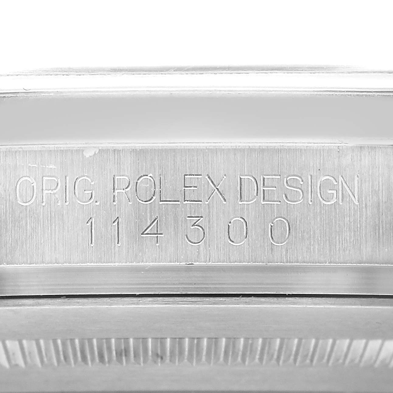 The image shows an engraving of "ORIG. ROLEX DESIGN 114300" on the case side of a Rolex Oyster Perpetual 114300 Men's Stainless Steel Black Dial watch.
