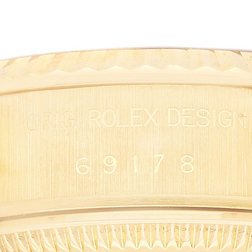 The image shows a close-up of the side of a Rolex President 69178 Women
s Yellow Gold Champagne Dial 69178 Women
s Yellow Gold Champagne Dial model case with engraved text and the edge of the bezel.