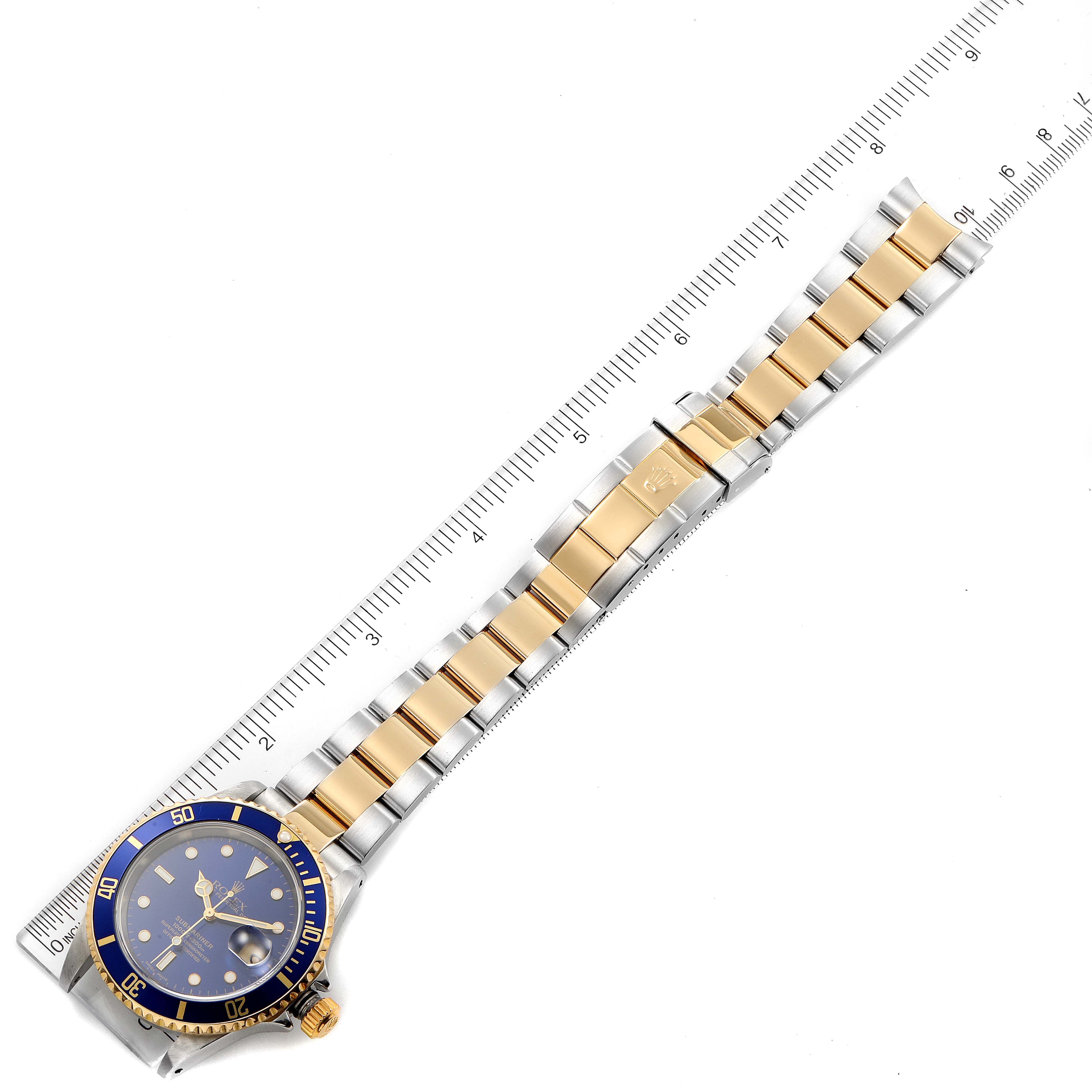 The image shows a Rolex Submariner 16613 Men
s Steel and Gold (two tone) Blue Dial 16613 Men
s Steel and Gold (two tone) Blue Dial watch laid flat with the bracelet fully extended alongside a ruler for measurement.