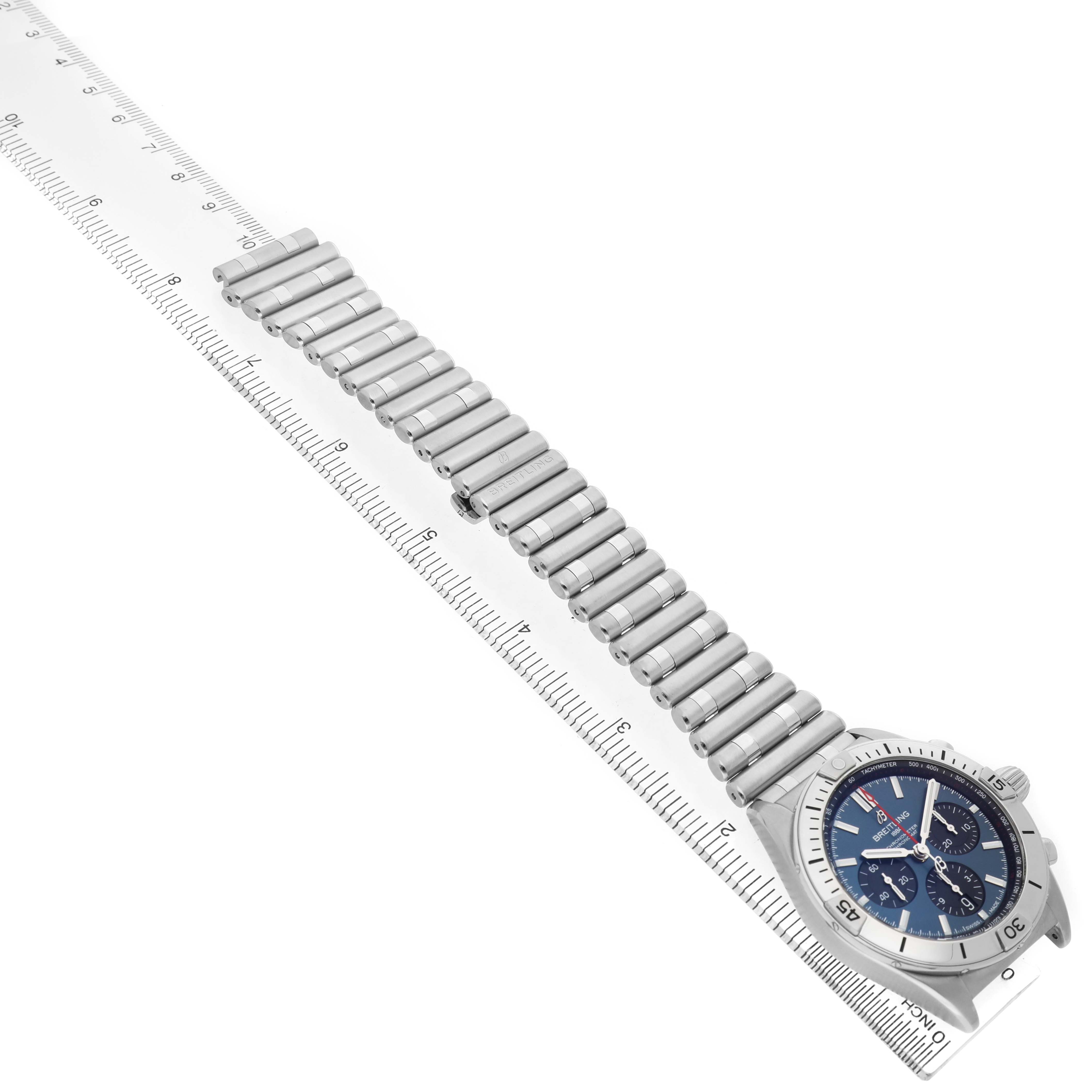 The Breitling Chronomat AB0134 Men's Stainless Steel Blue Dial watch is shown diagonally, showcasing the face and full metal bracelet alongside a ruler.
