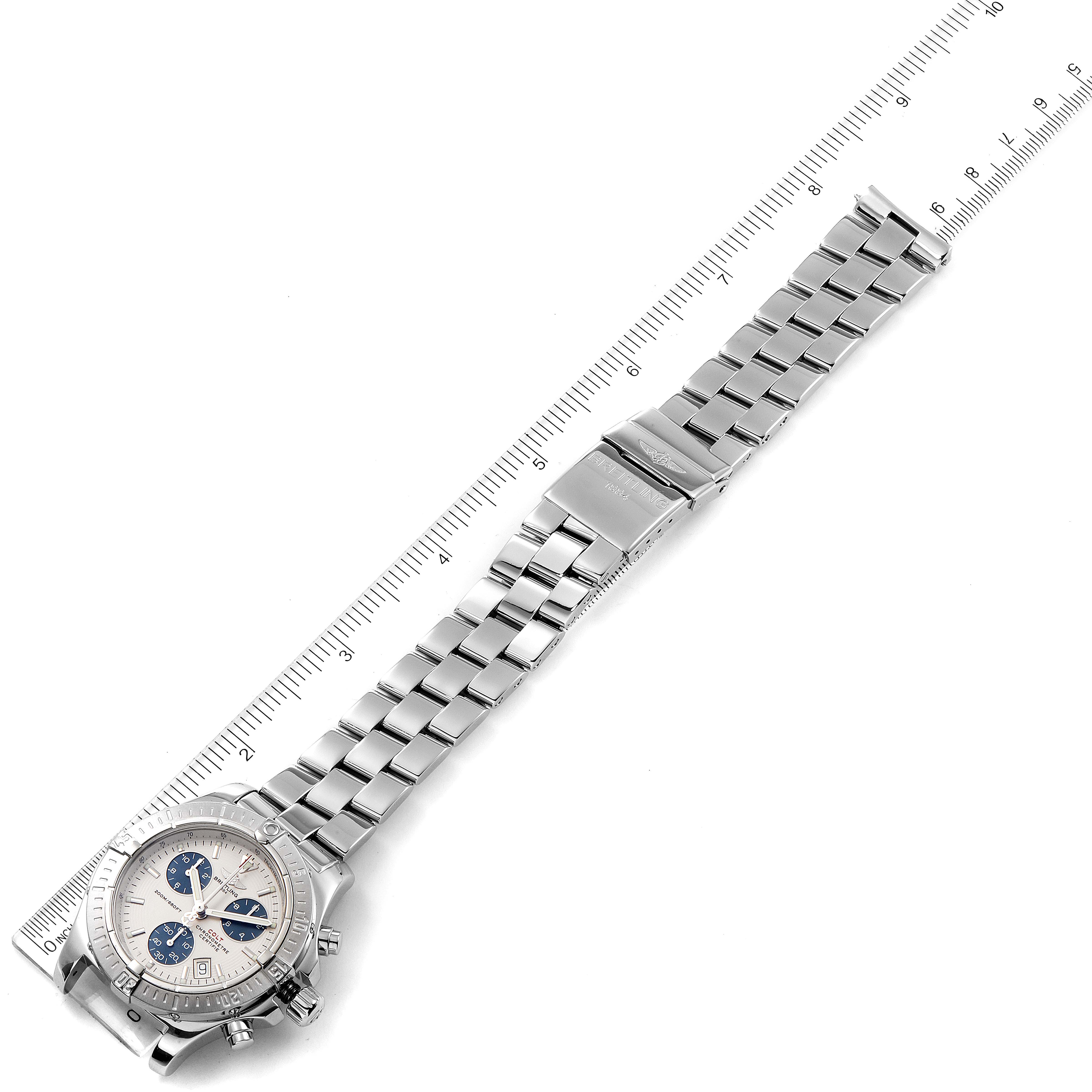 The image shows a Breitling Colt A73380 Men
s Stainless Steel White Dial A73380 Men
s Stainless Steel White Dial watch with its full metal bracelet, positioned next to a ruler, captured from an overhead angle.