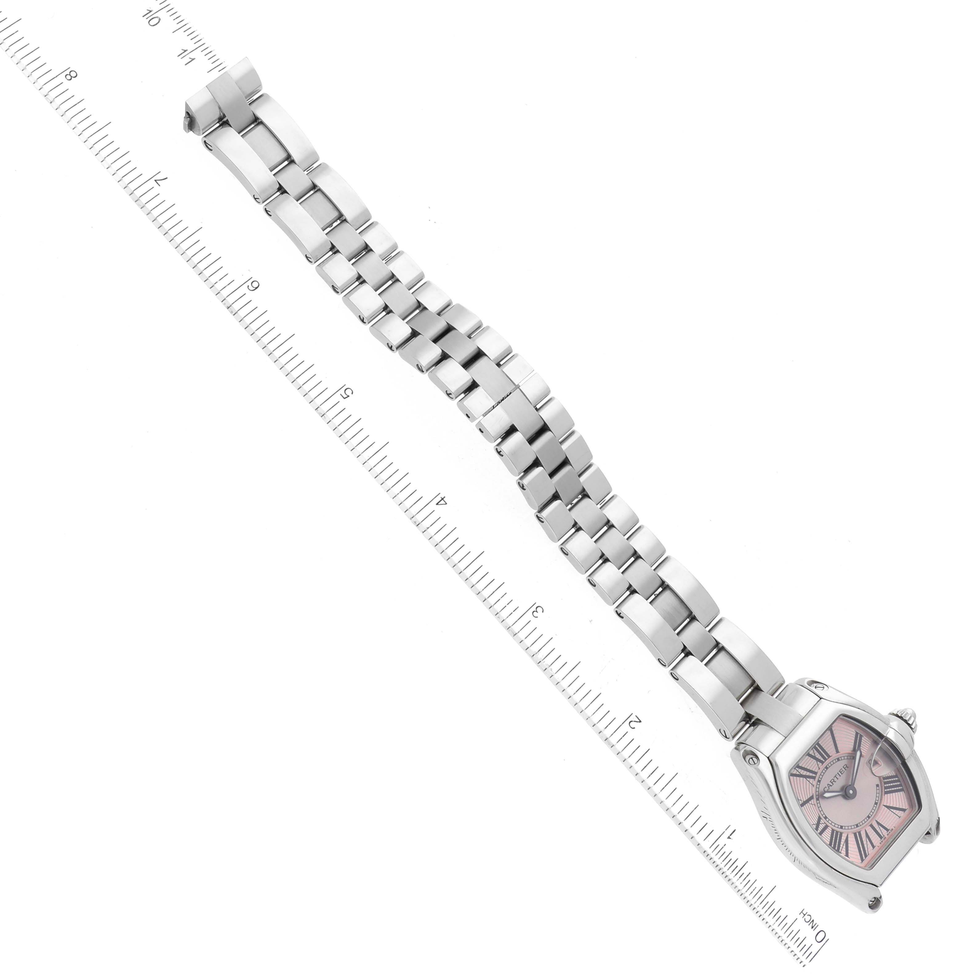 The image shows the Cartier Roadster W62017V3 Women's Stainless Steel Pink Dial W62017V3 Women's Stainless Steel Pink Dial watch laid flat with its face and full bracelet on display next to a ruler for scale.