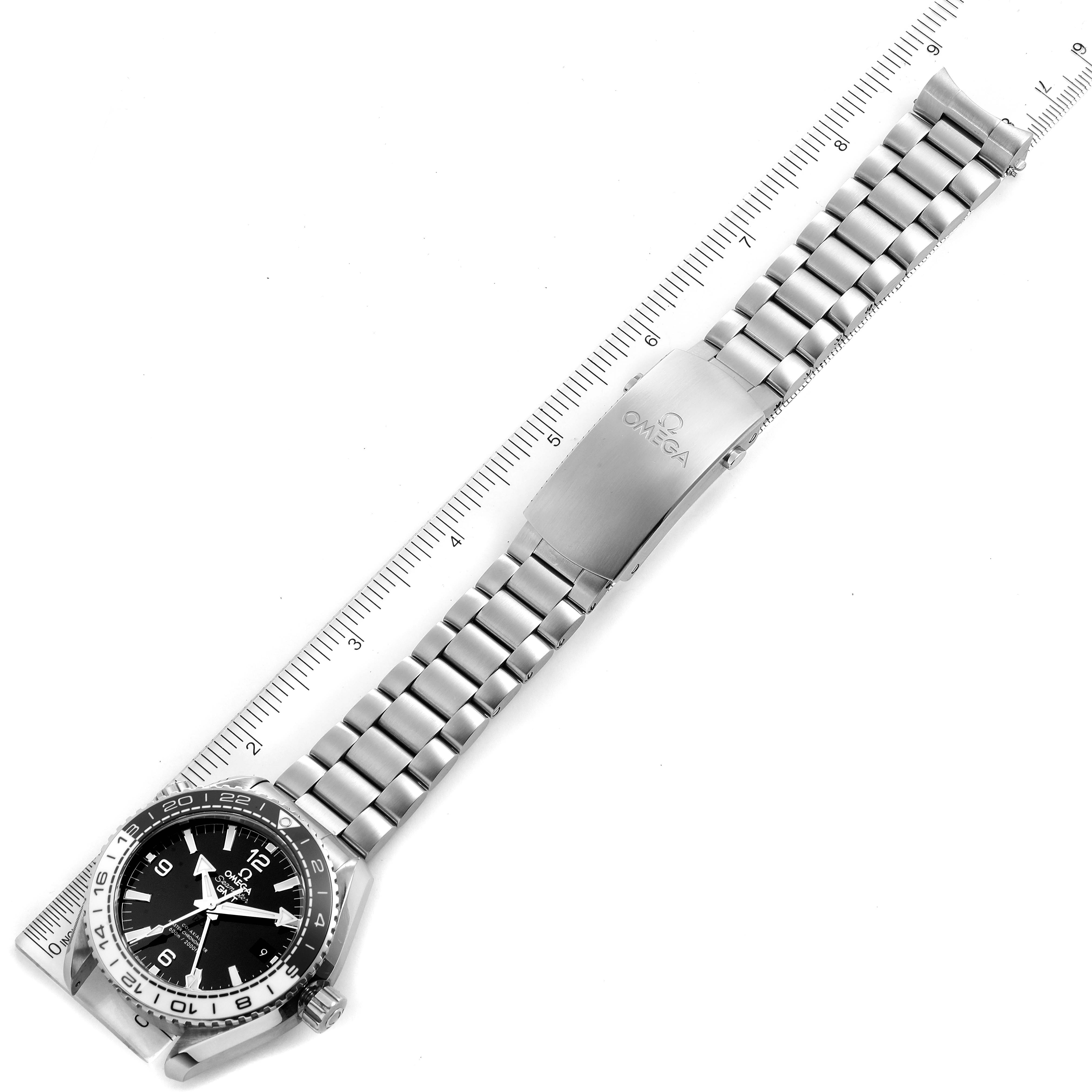 The image shows an overhead view of the Omega Planet Ocean 215.30.44.22.03.001 Men
s Stainless Steel Black Dial 215.30.44.22.03.001 Men
s Stainless Steel Black Dial watch, displaying the face, bracelet, and clasp next to a ruler.