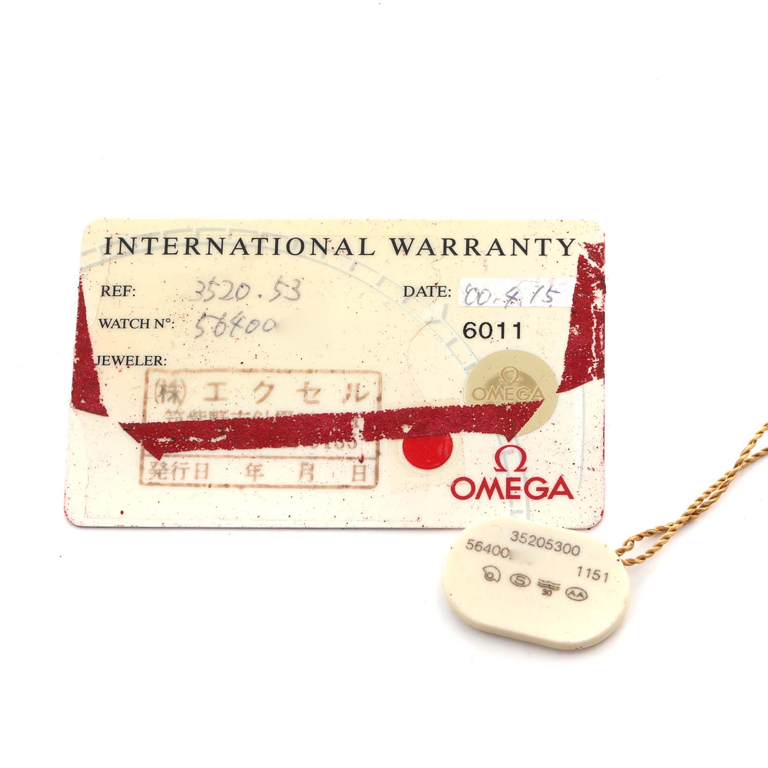 The image shows an Omega Speedmaster 3520.53.00 Men
s Stainless Steel Grey Dial 3520.53.00 Men
s Stainless Steel Grey Dial International Warranty card and a small Omega tag, both viewed from above.