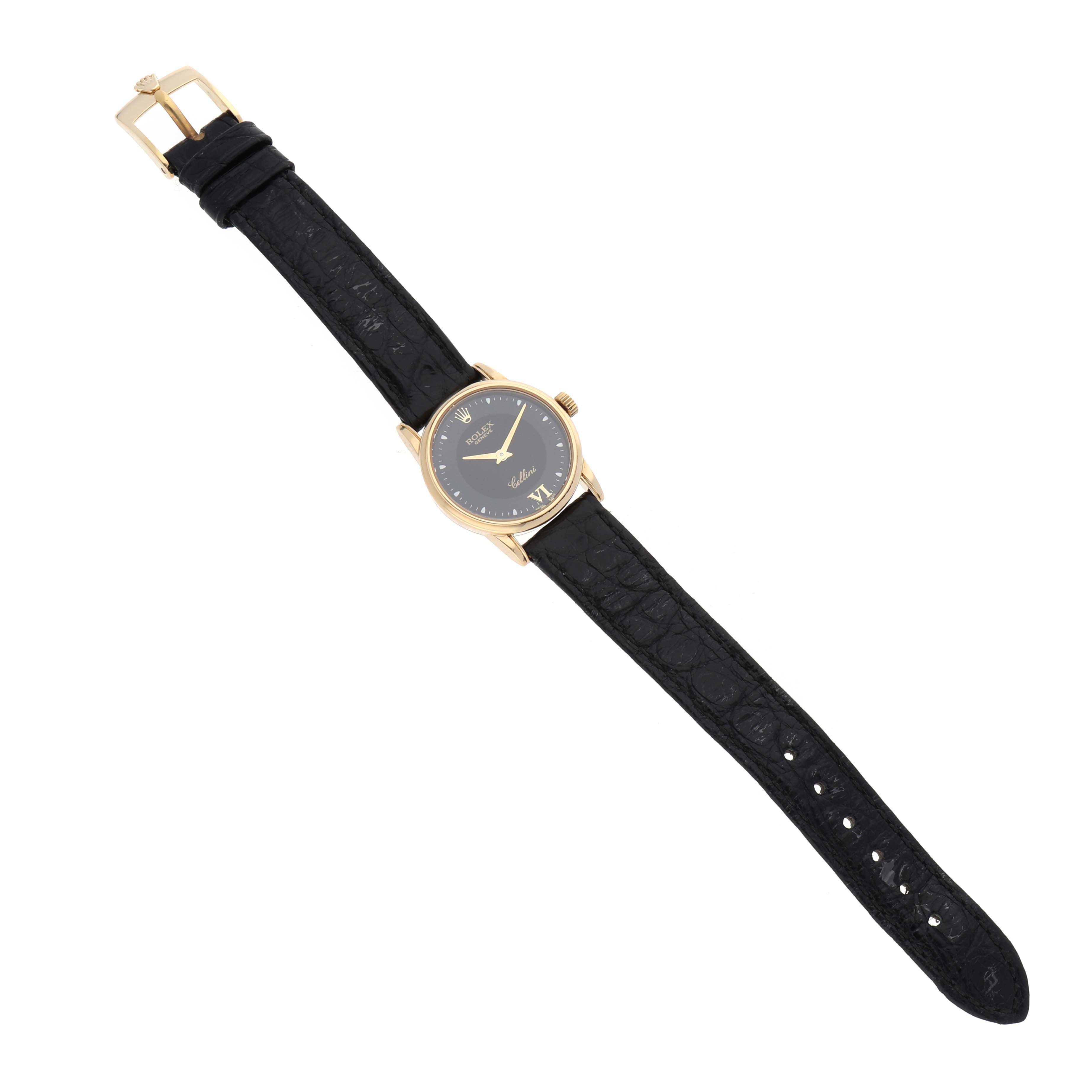 The Rolex Cellini 6111/8 Women
s Yellow Gold Black Dial 6111/8 Women
s Yellow Gold Black Dial watch is shown from a top-down angle, displaying its black strap, gold case, and black dial.