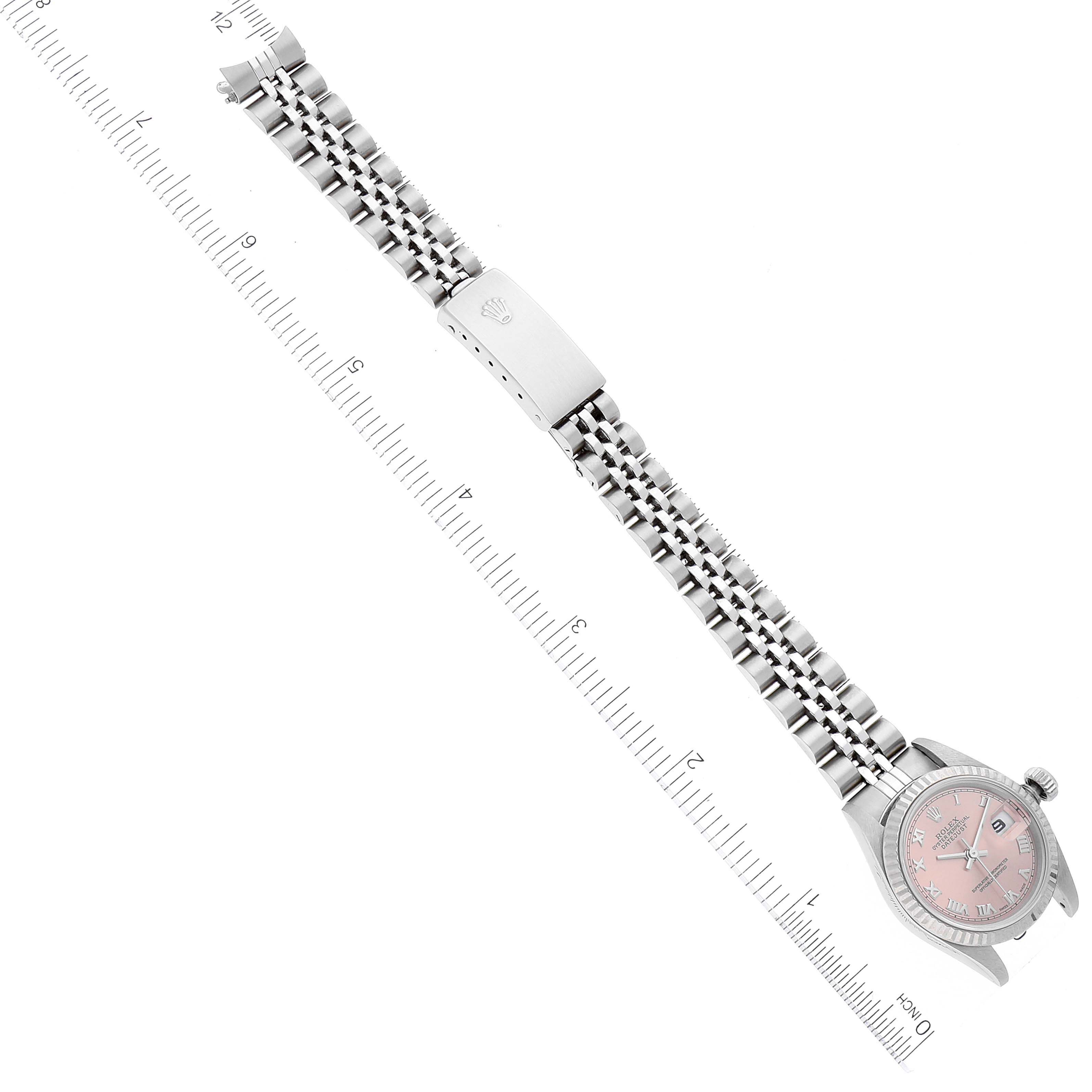 The Rolex Datejust 79174 Women
s Stainless Steel Pink Dial 79174 Women
s Stainless Steel Pink Dial watch is shown from above, displaying the full bracelet, clasp, and dial with a pink face next to a ruler.