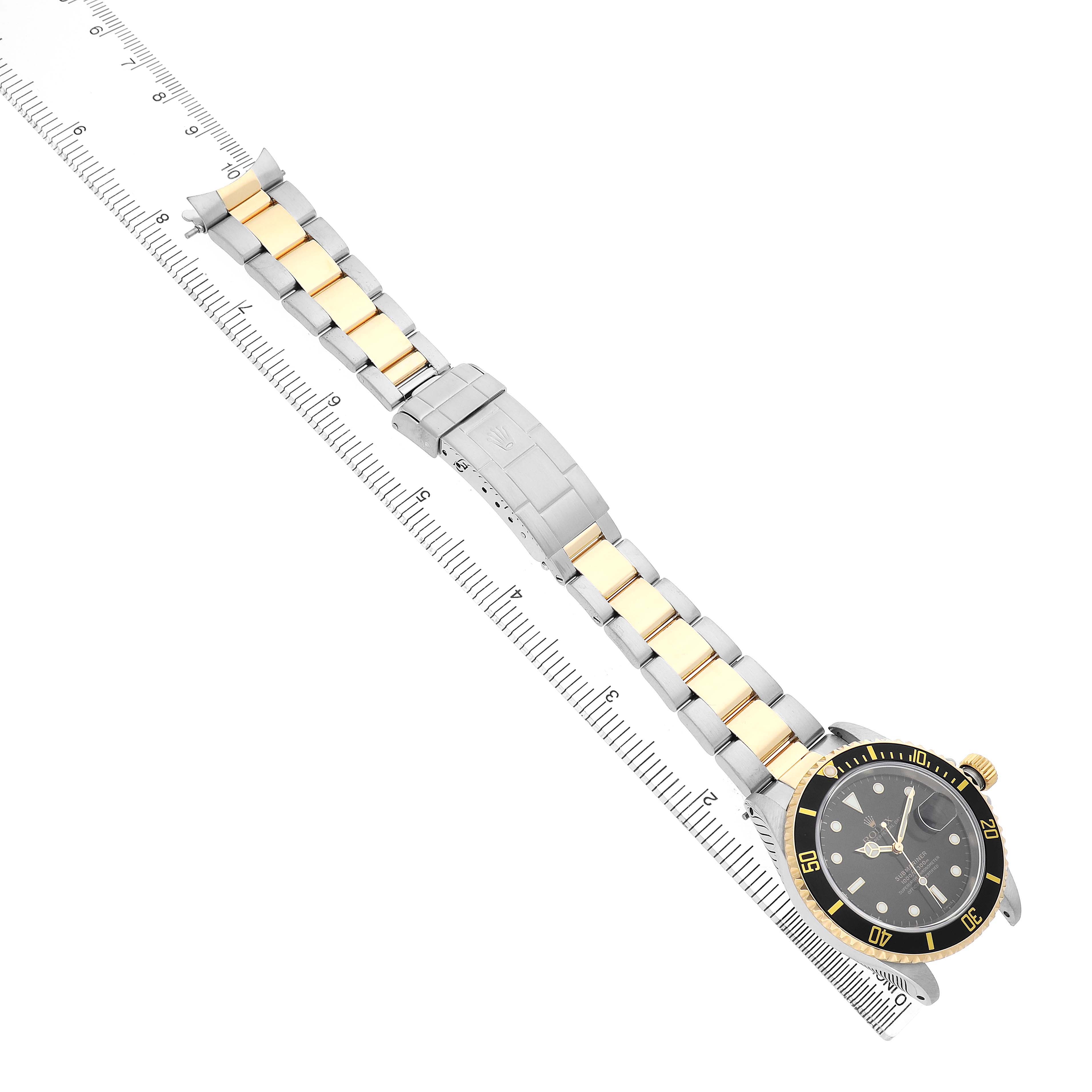 The Rolex Submariner 16613 Men's Steel and Gold (two tone) Black Dial watch is shown at a diagonal angle, displaying the bracelet and watch face next to a measuring ruler.