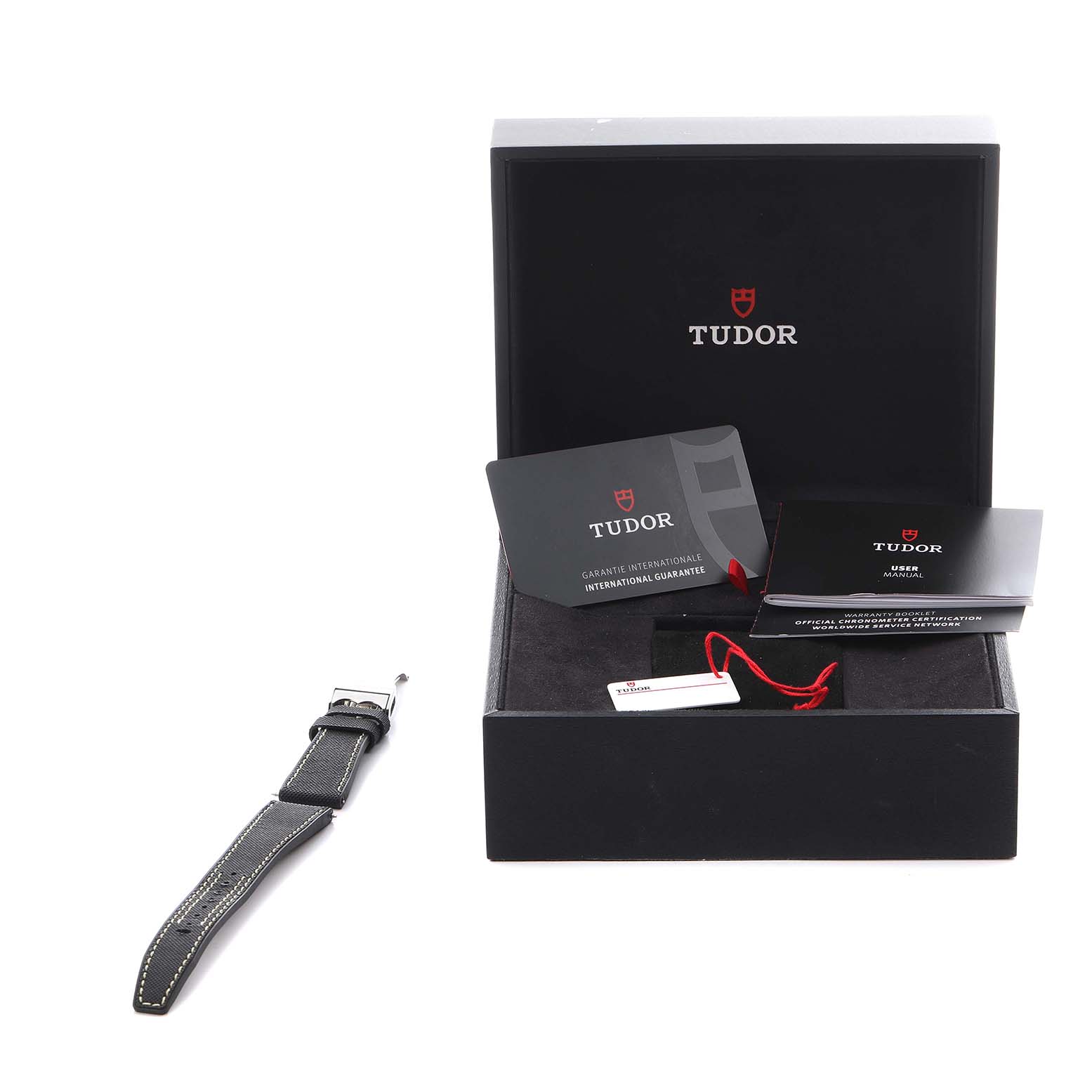 The image shows a Tudor Heritage Black Bay 79470 Men
s Stainless Steel Black Dial 79470 Men
s Stainless Steel Black Dial watch box, manuals, warranty card, and a detached strap from a front angle.