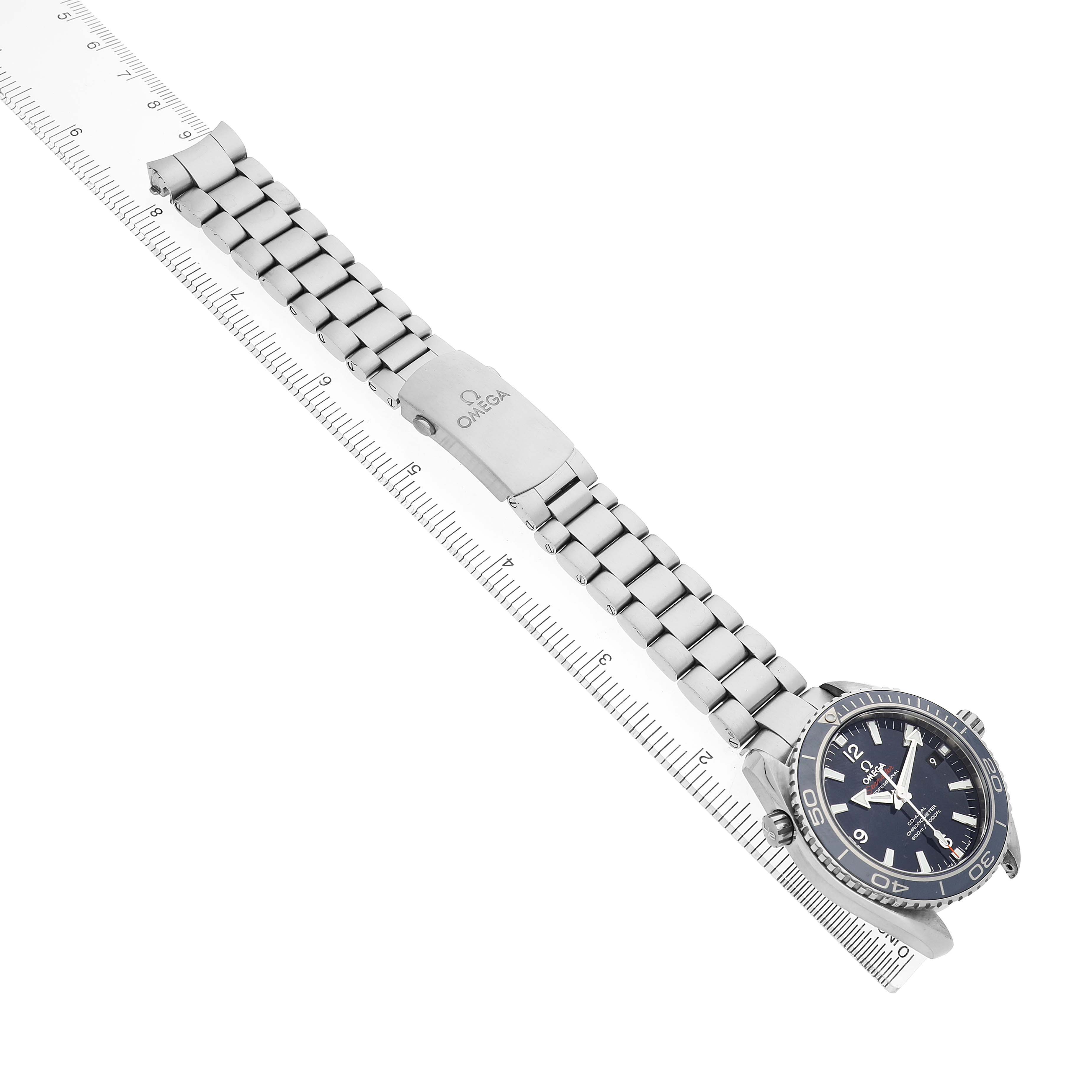 The Omega Seamaster 232.90.42.21.03.001 Men's Titanium Blue Dial watch is shown at an angle, displaying the face, bezel, and metal bracelet alongside a measuring ruler.