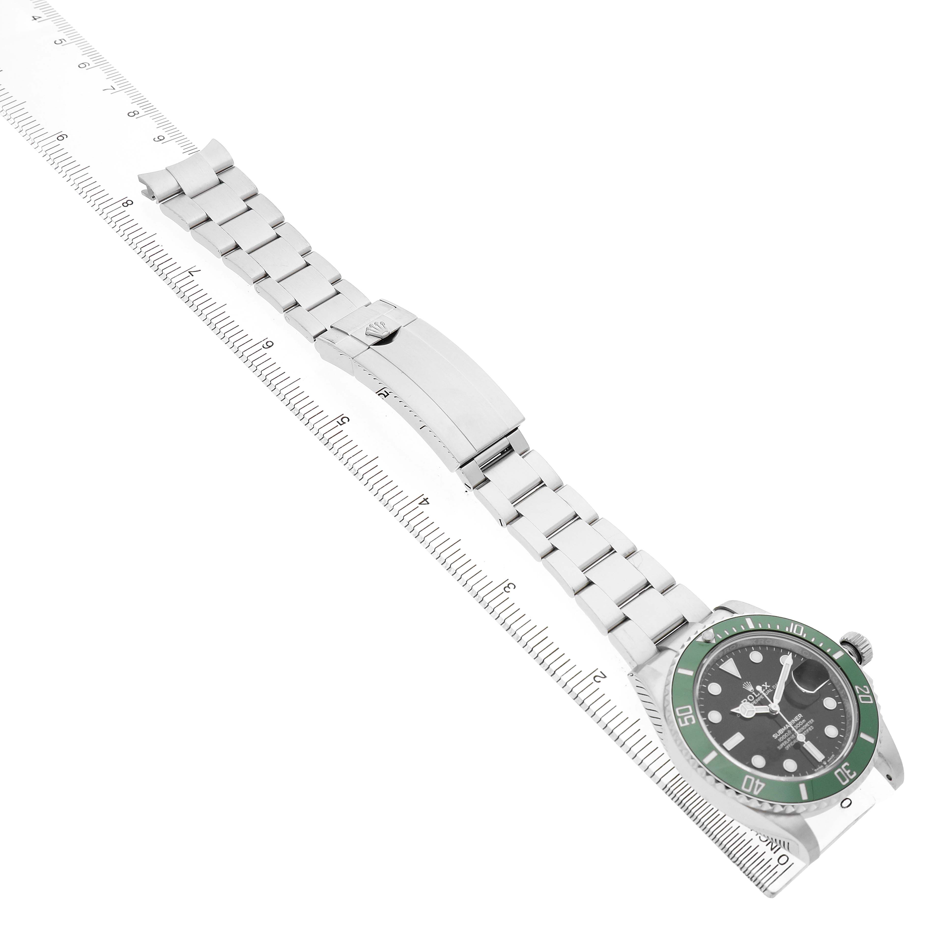 The Rolex Submariner M126610LV-0002 Men's Stainless Steel Black Dial watch is shown from an angled top view, displaying the dial, bezel, bracelet, and clasp beside a ruler.