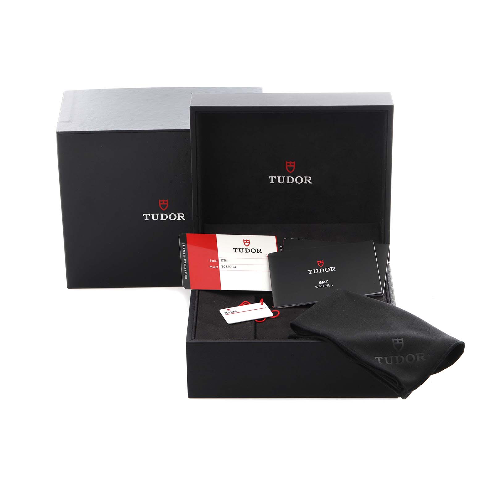 The image shows packaging and accessories for the Tudor Heritage Black Bay 79830RB Men
s Stainless Steel Black Dial 79830RB Men
s Stainless Steel Black Dial, including a box, manual, tag, and cloth.