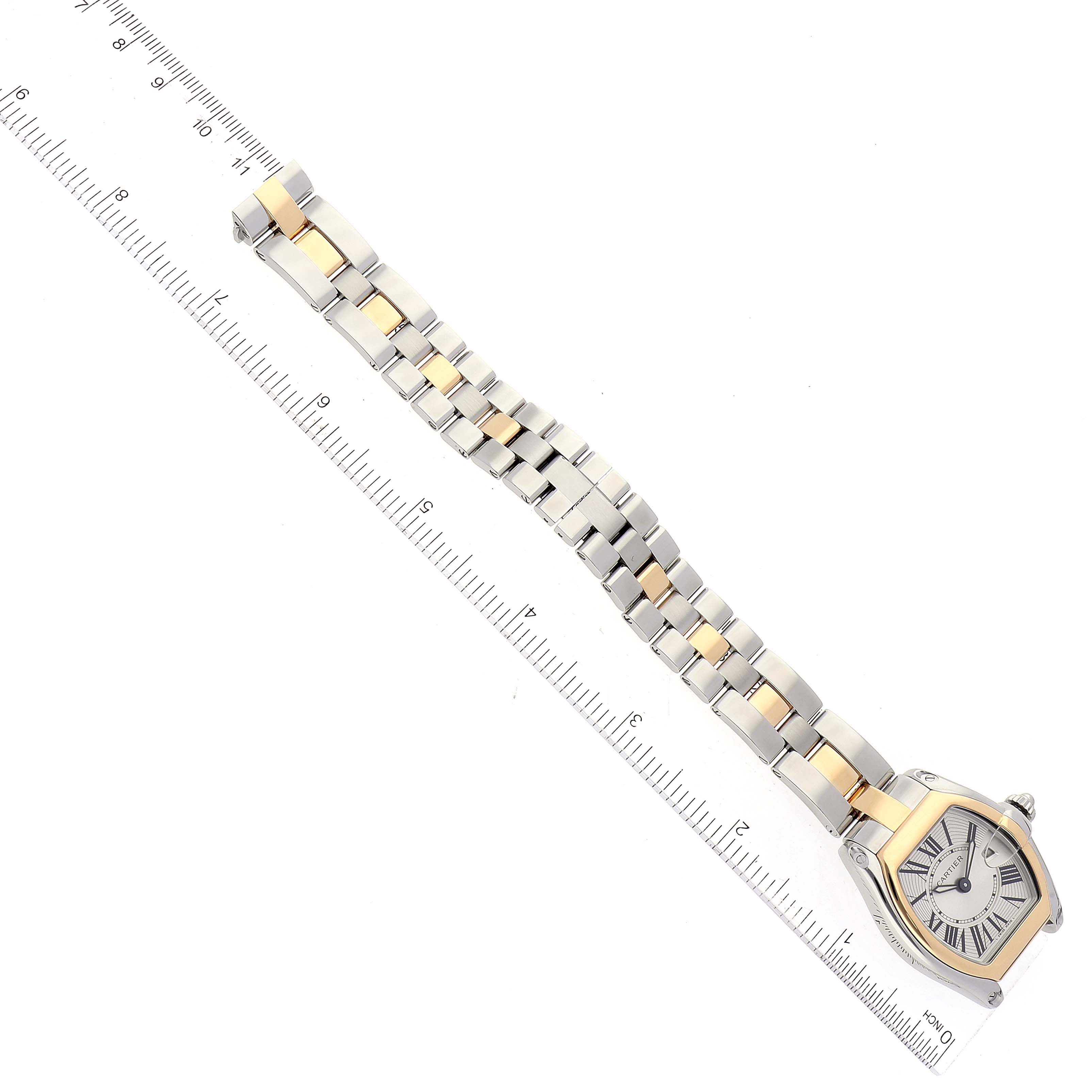 The Cartier Roadster W62026Y4 Women's Steel and Gold (two tone) Silver Dial W62026Y4 Women's Steel and Gold (two tone) Silver Dial watch is shown from a top-down angle, highlighting its face, two-tone bracelet, and a ruler beside it.