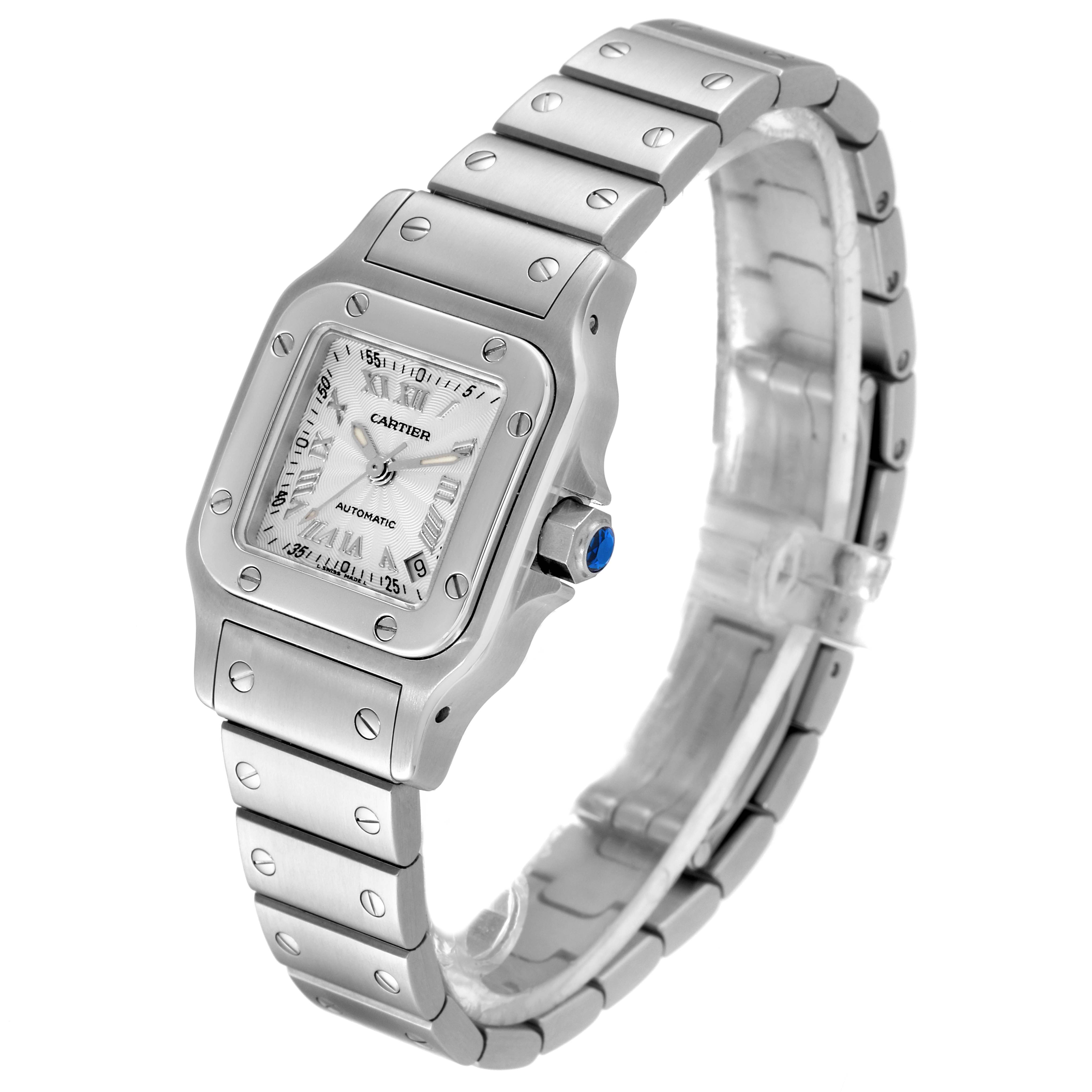 The Santos model by Cartier is shown from a three-quarter angle, displaying the face, bezel, bracelet, and crown with a blue gem.