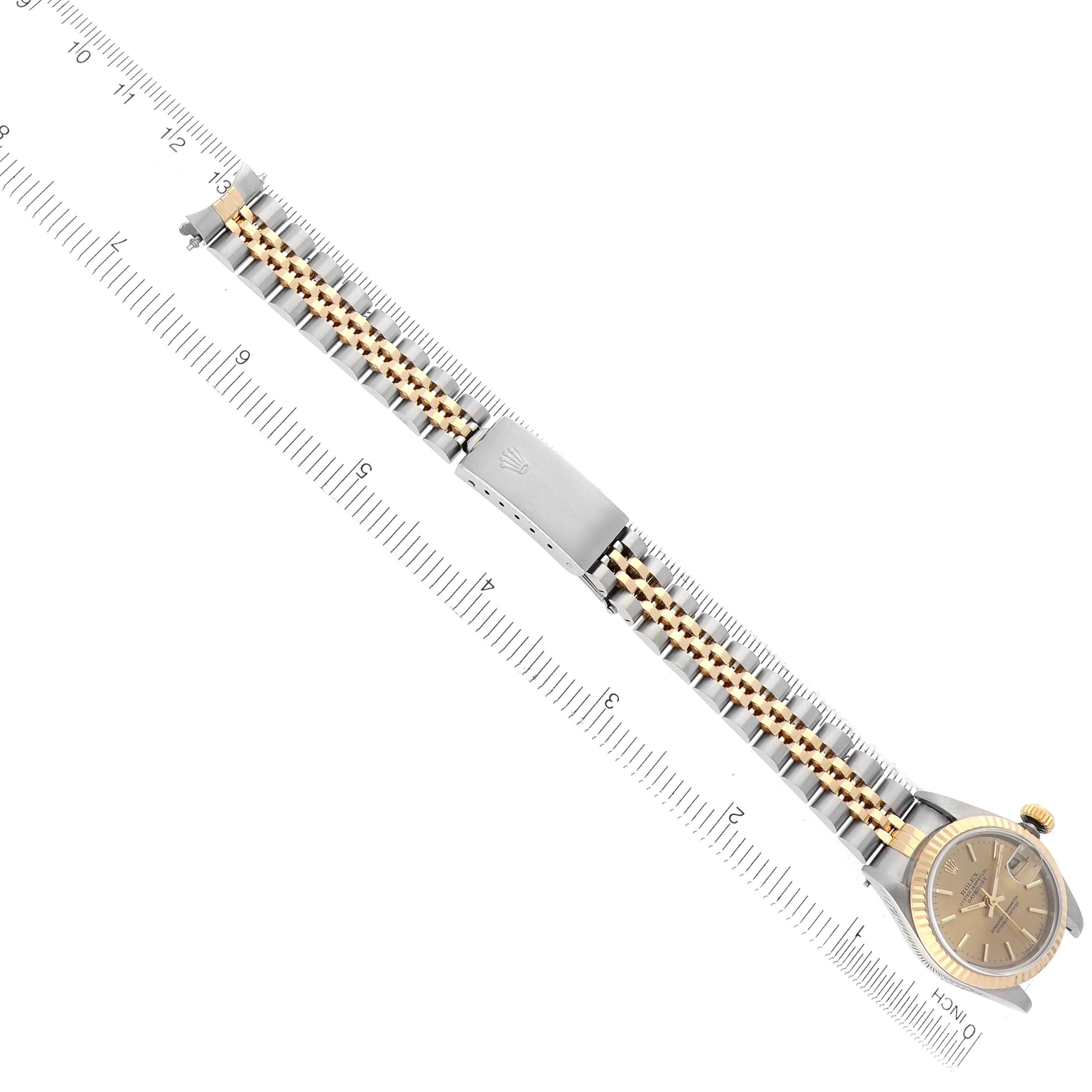 The Rolex Datejust 69173 Women
s Steel and Gold (two tone) Champagne Dial 69173 Women
s Steel and Gold (two tone) Champagne Dial watch is shown from a top view, highlighting the face, bracelet, and clasp against a measuring ruler.